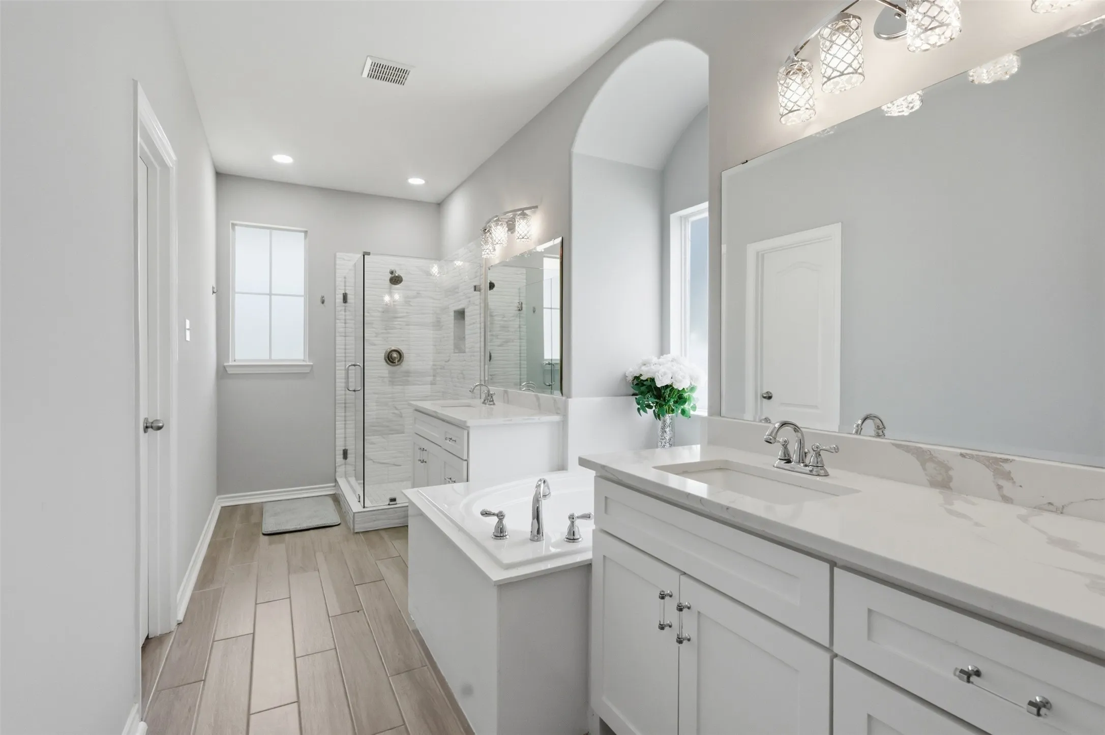 Spacious bathroom featuring wood-finish tile flooring, a built-in soaking tub, and a glass-enclosed shower with tile surround