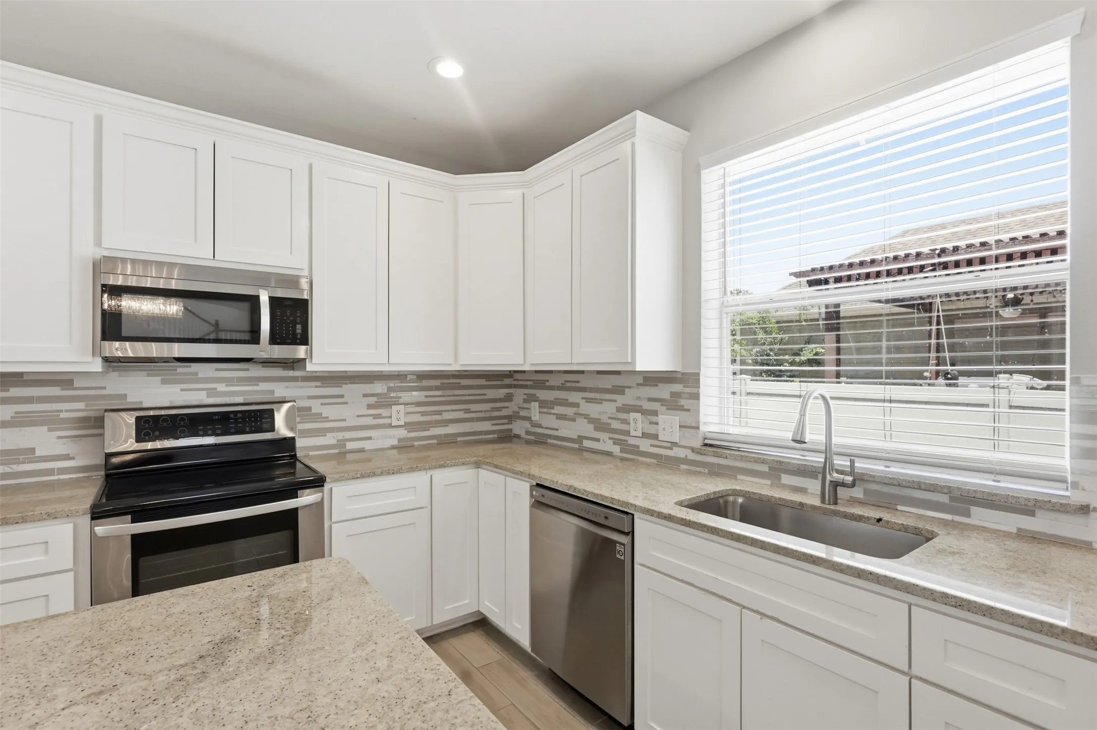 Bright kitchen featuring white shaker cabinetry, light-toned countertops, stainless steel appliances, a tile backsplash, and an undermount sink with a gooseneck faucet