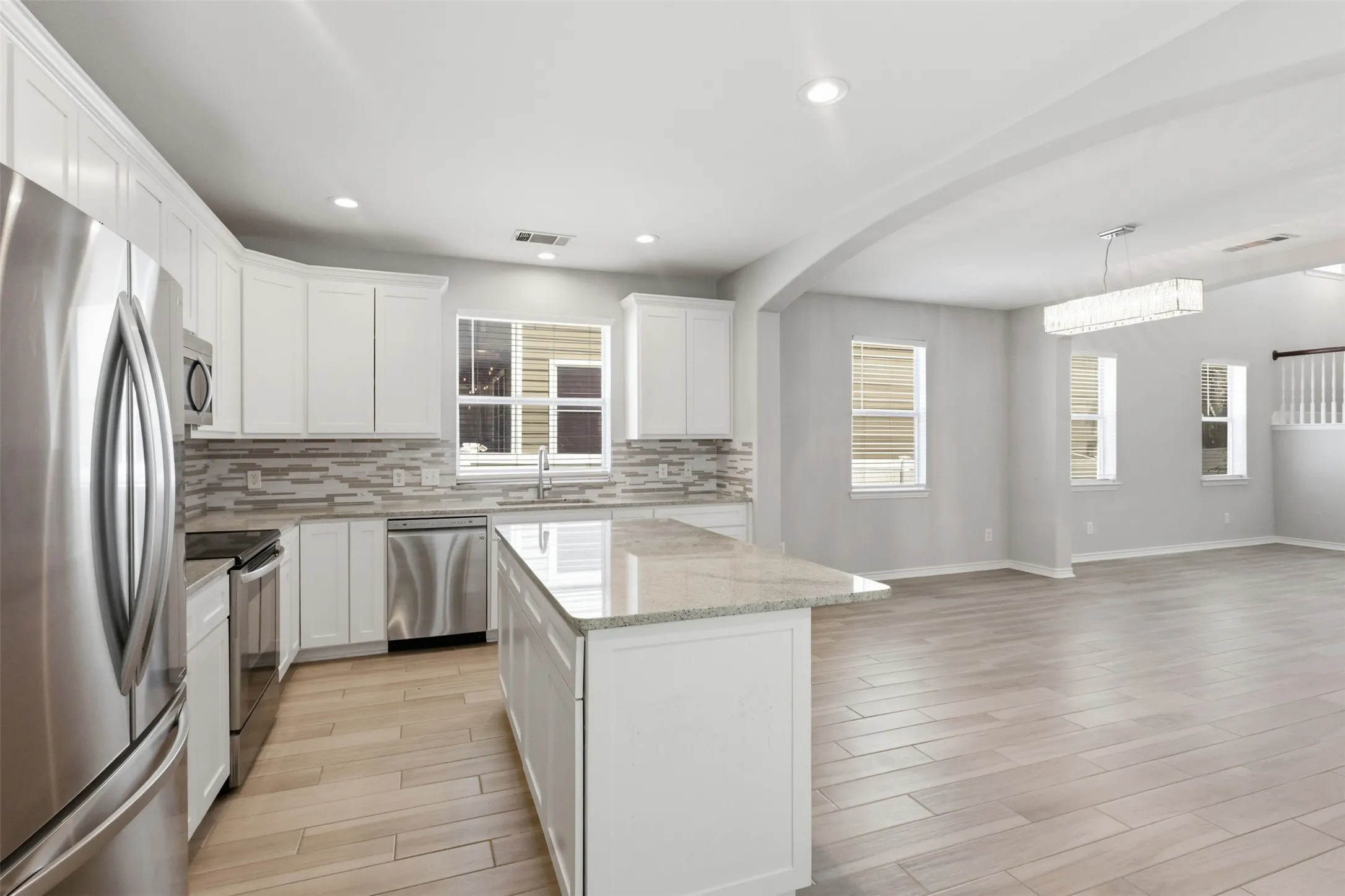 Kitchen featuring white cabinetry, stainless steel appliances, a light-toned tile backsplash, and a center island with a light granite-finish countertop