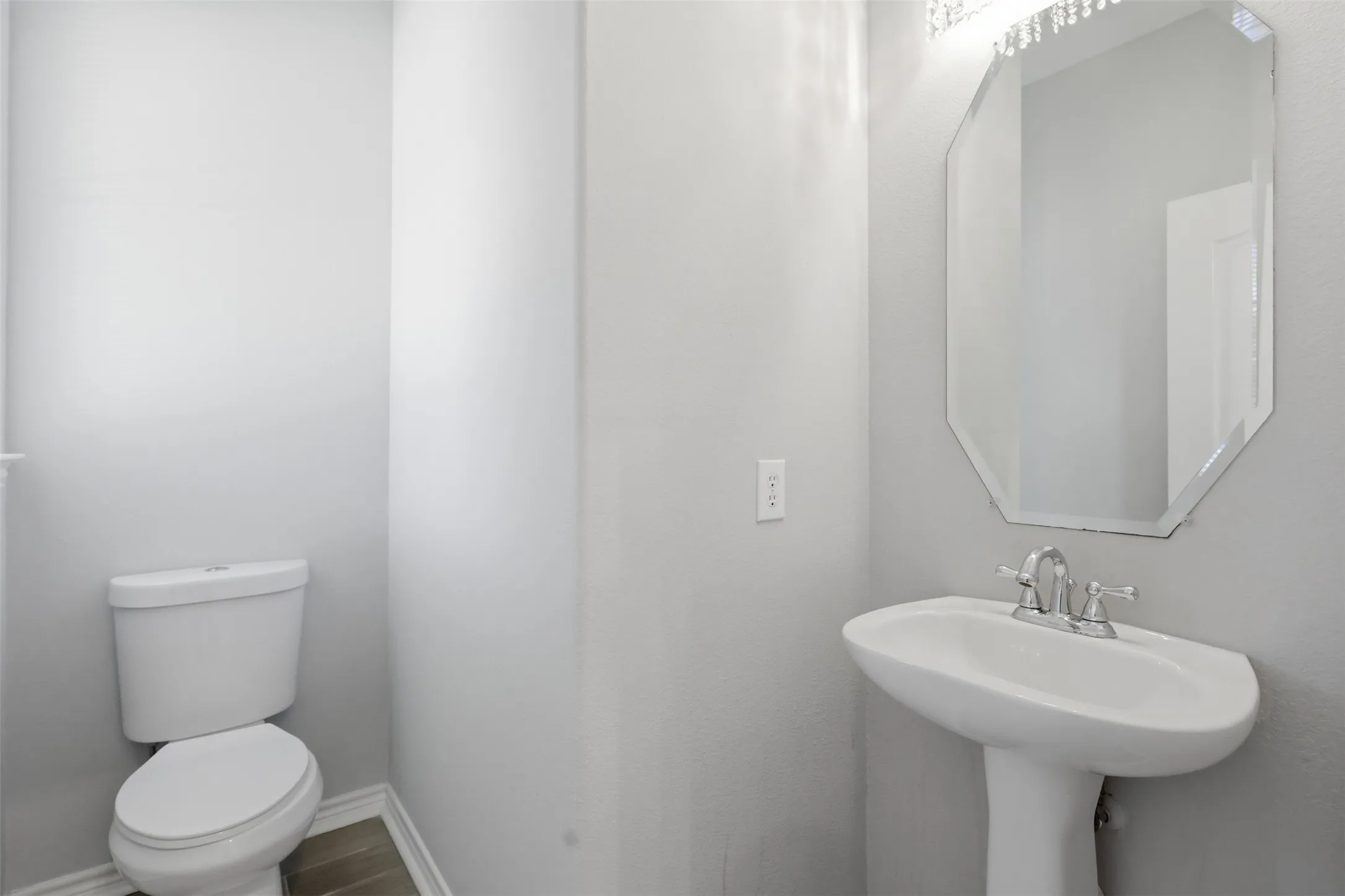 Pedestal sink with chrome faucet, octagonal mirror, and a crystal-accented vanity light