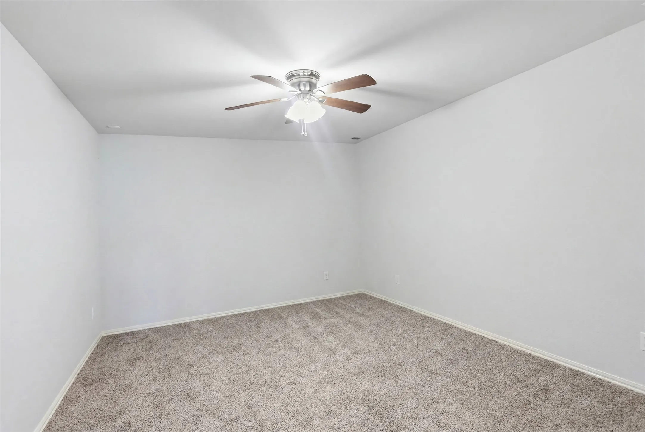 Spacious room with light neutral wall tones, textured carpeting, and a ceiling fan with integrated lighting