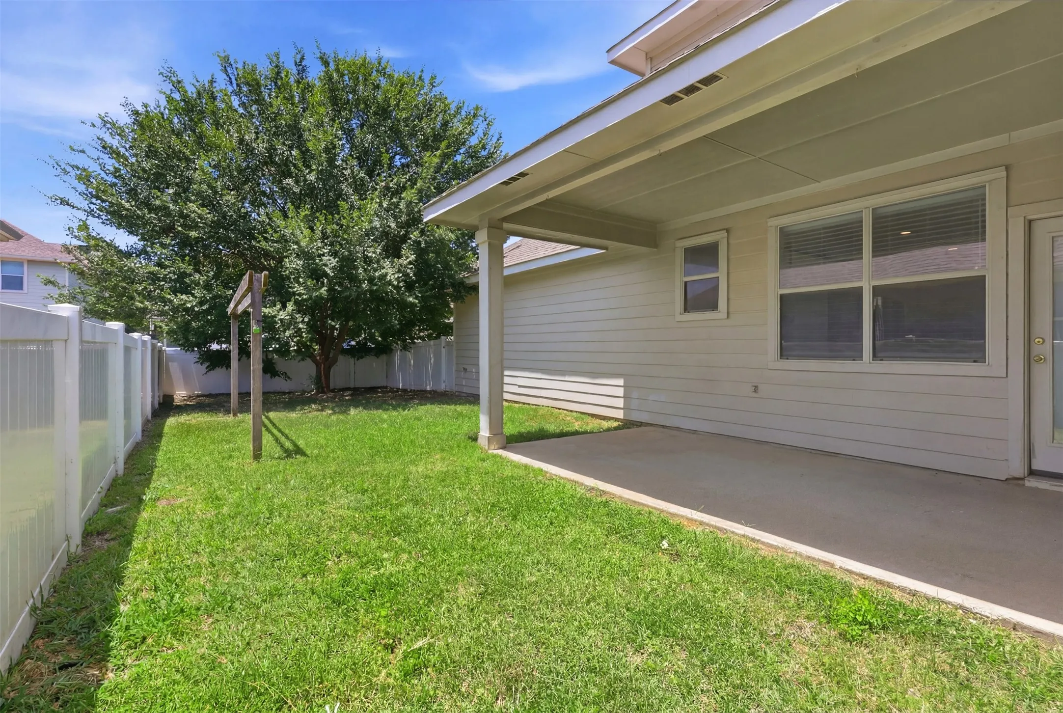 Expansive backyard with a large shade tree, white privacy fencing, covered patio, and concrete slab