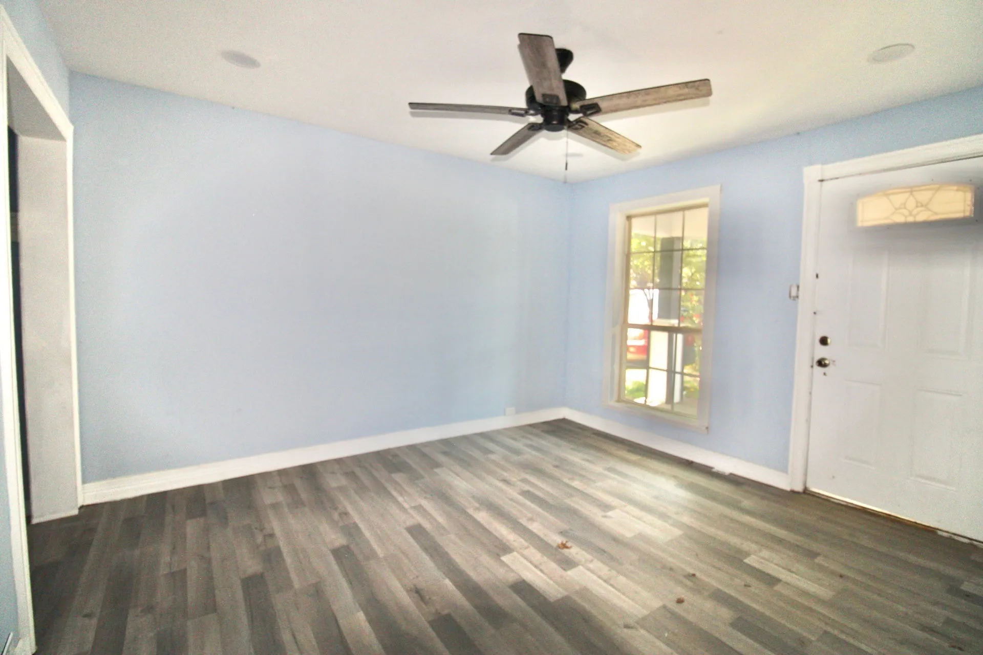 Room featuring wood-finish flooring, a ceiling fan, light blue walls, and white baseboards