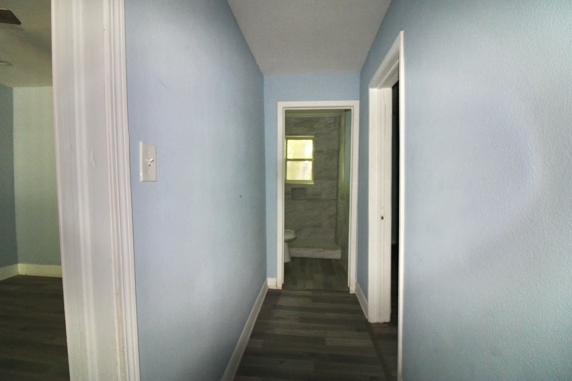 Hallway featuring wood-finish flooring, light blue wall paint, and white trim
