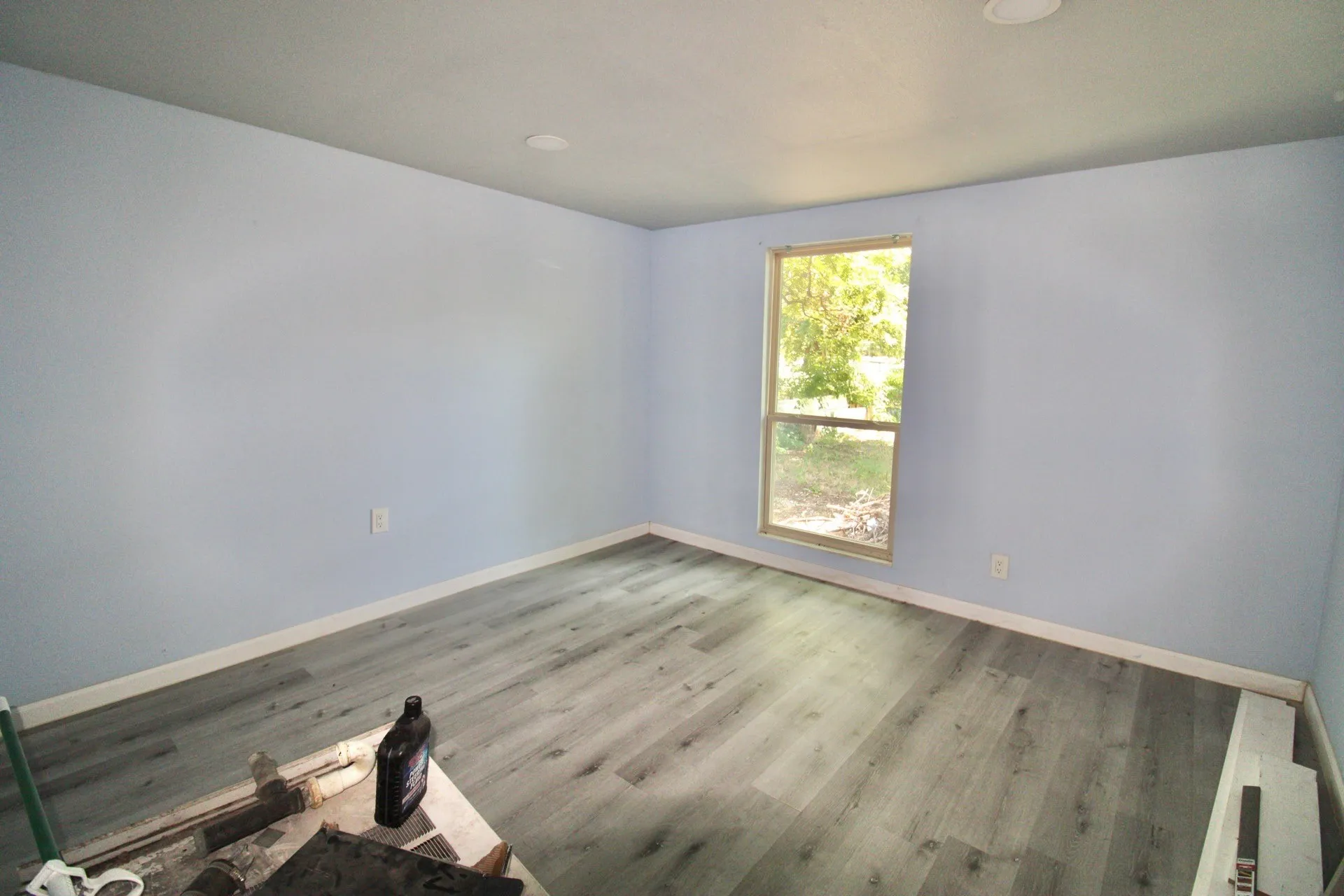 Spacious room featuring light blue walls, recessed lighting, white baseboards, and wood-finish flooring