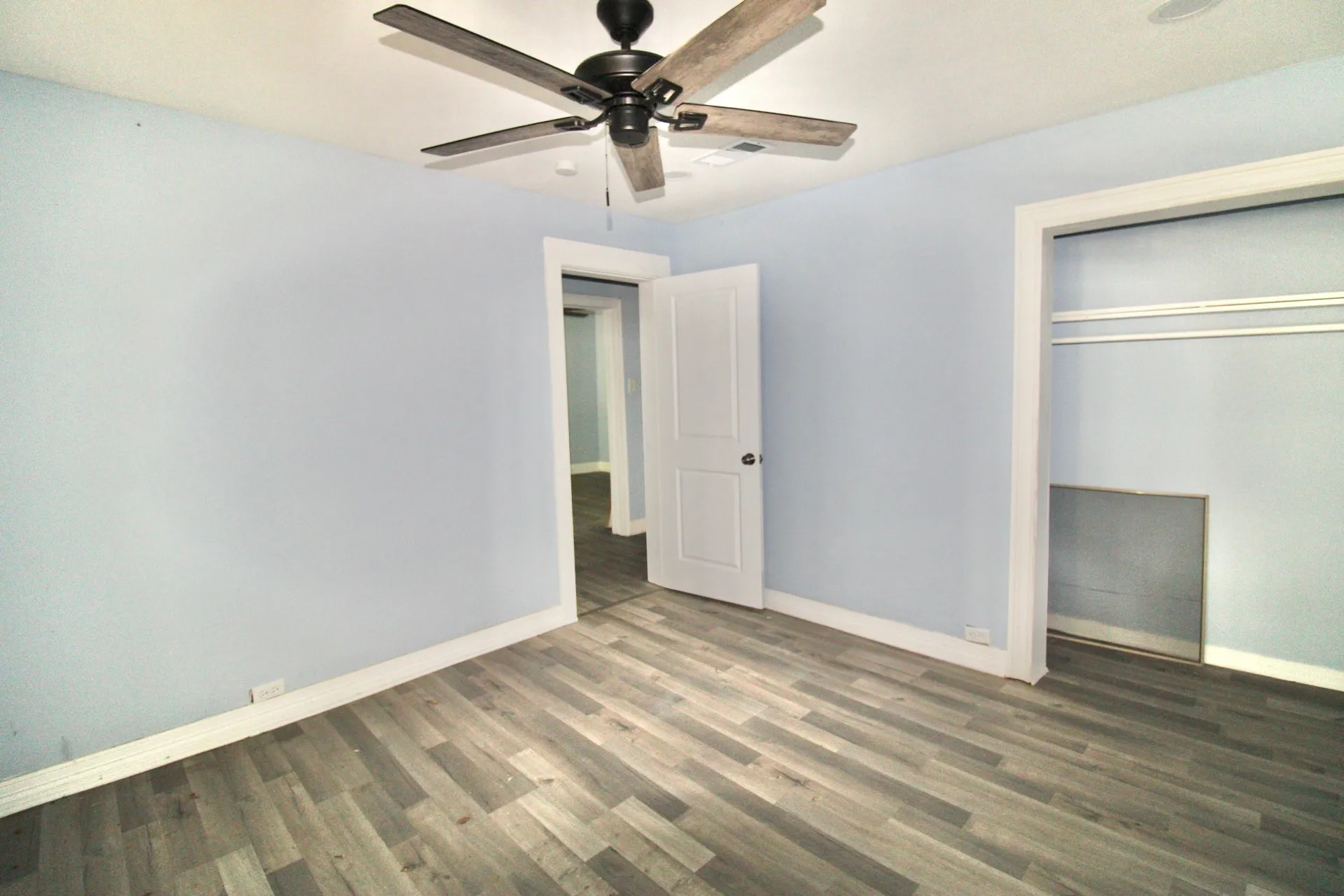 Interior room featuring wood-finish flooring, light blue wall paint, white trim, and a ceiling fan with integrated lighting