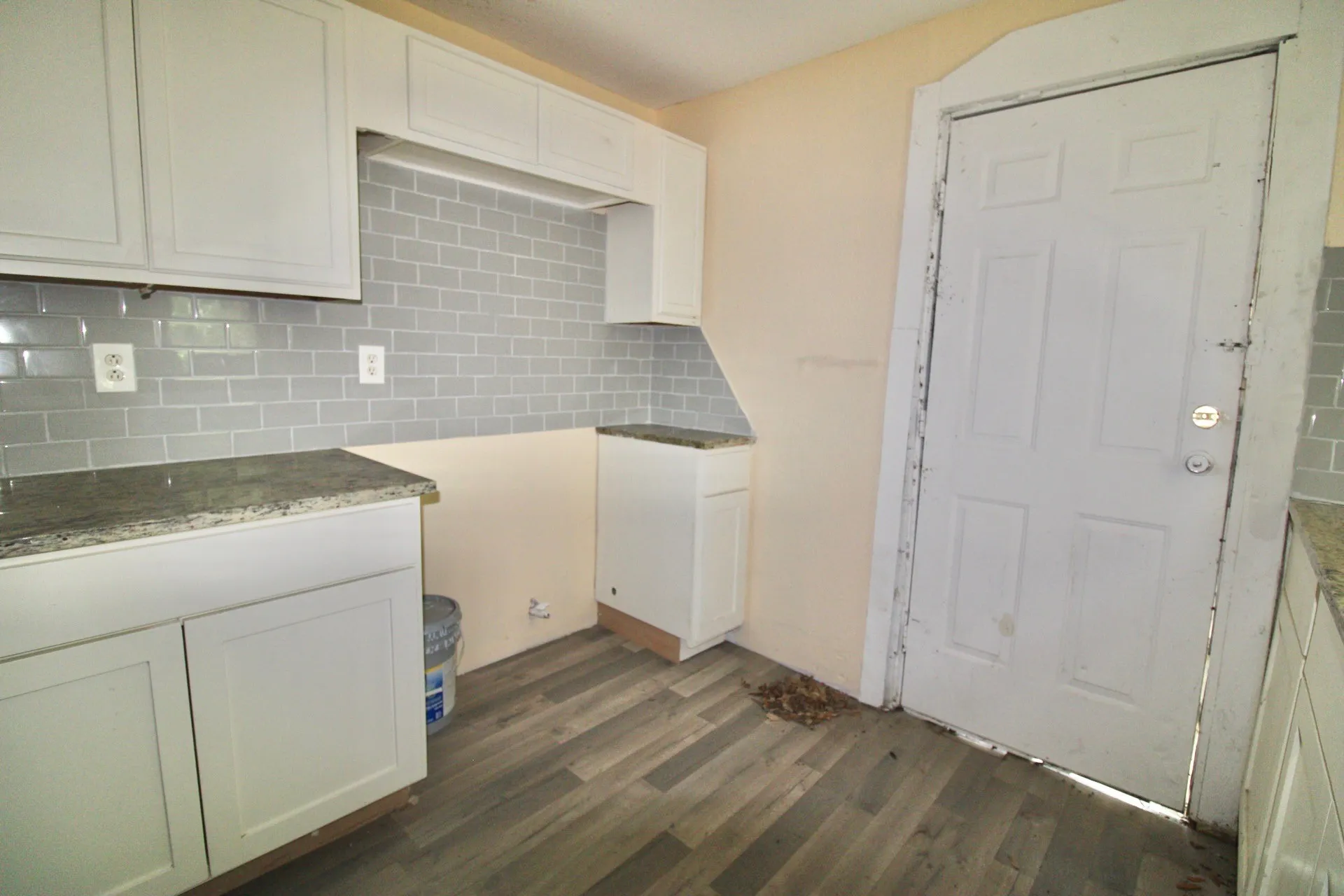 Kitchen area featuring light gray subway tile backsplash, white cabinetry, speckled countertops, and wood-finish flooring