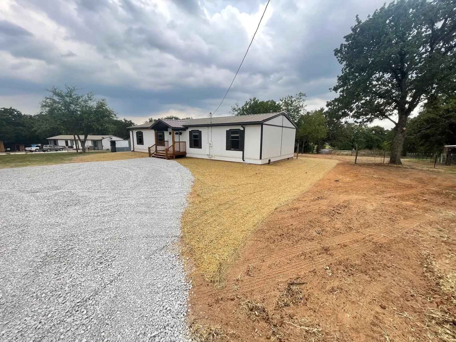 White exterior with dark trim accents, featuring a gravel driveway and a natural wood-finish front porch