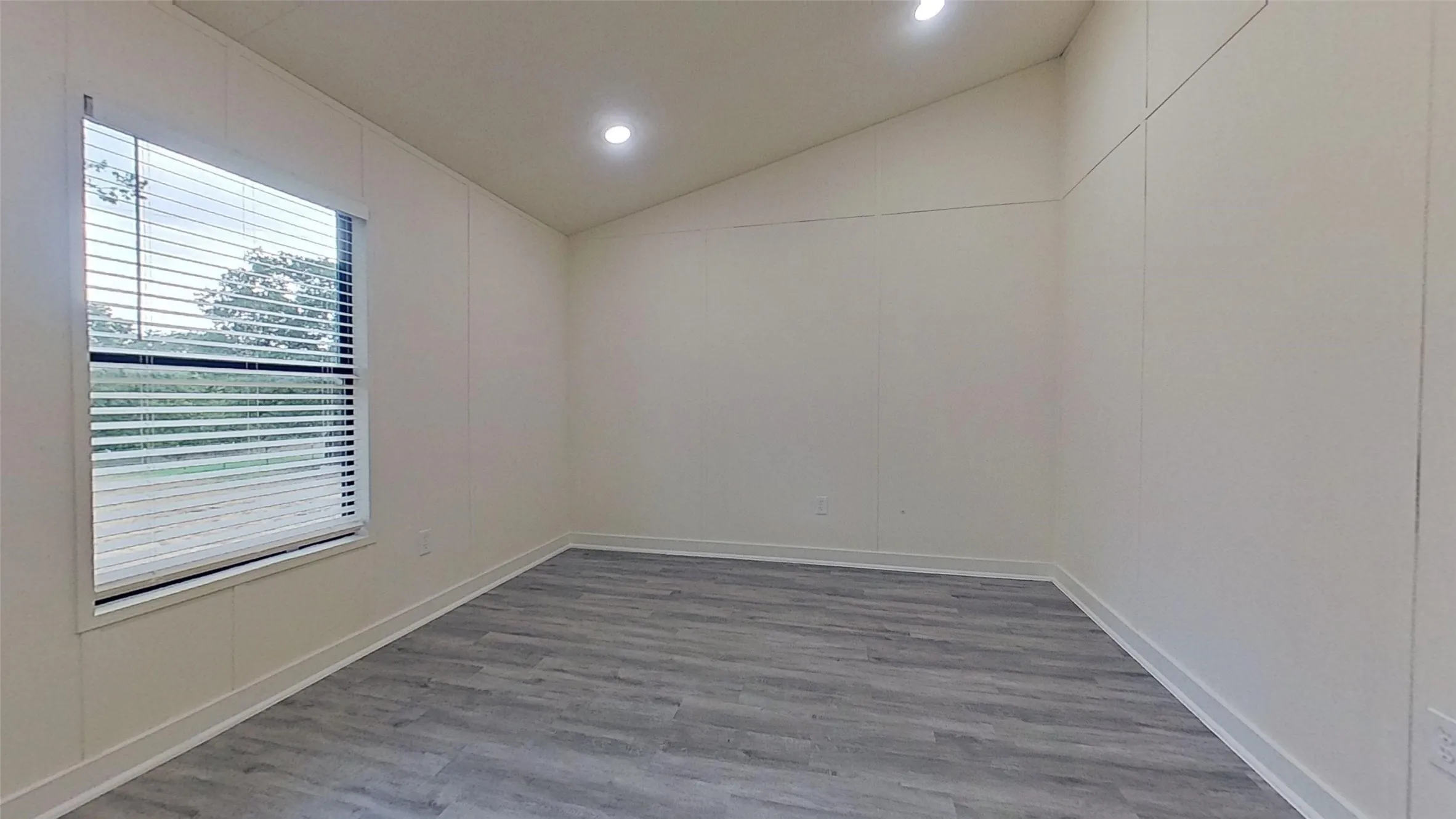 Room featuring wood-finish flooring, white paneled walls, and a vaulted ceiling with recessed lighting