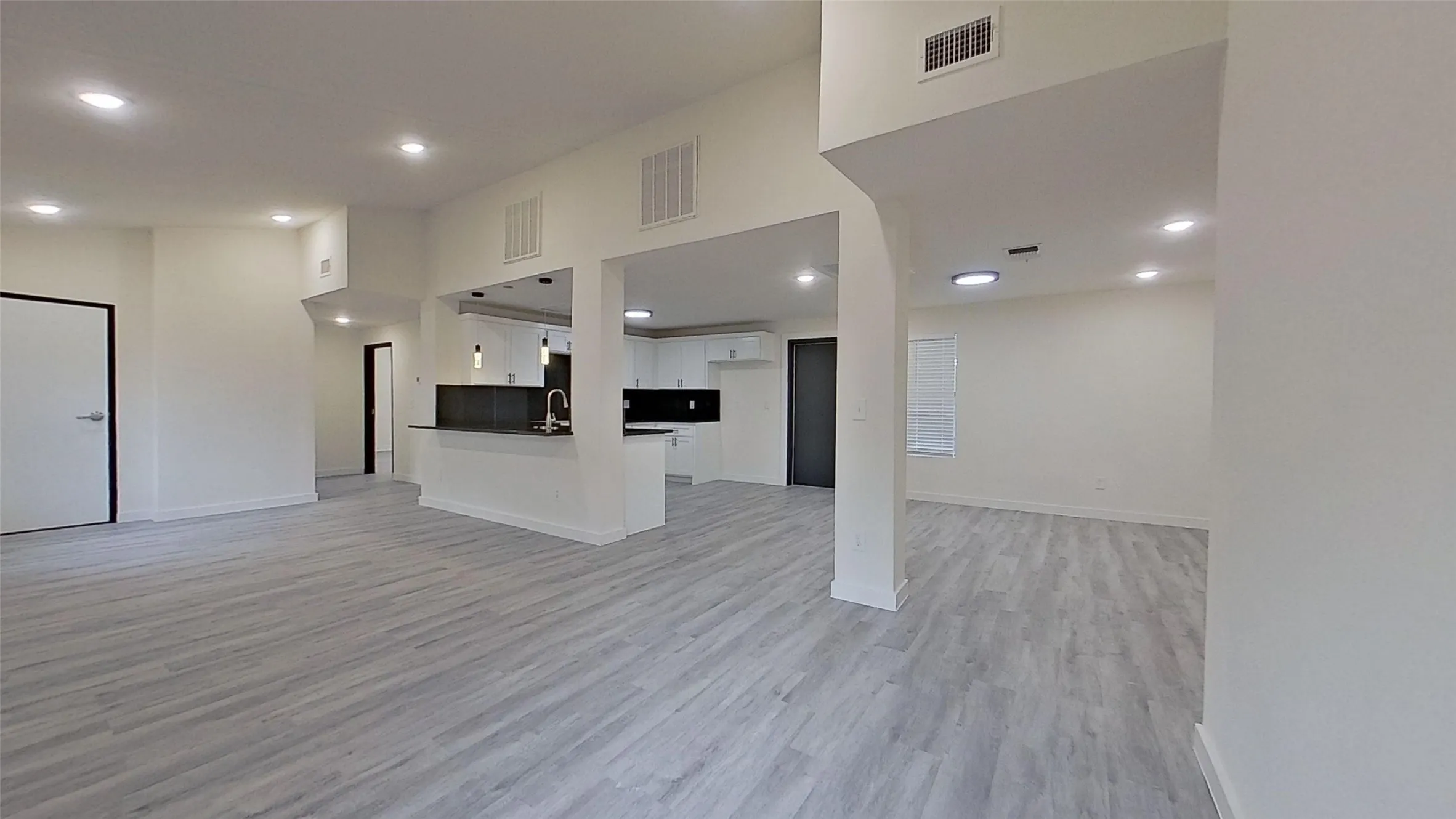 Open-concept interior featuring light wood-finish flooring throughout, recessed lighting, and a kitchen with white cabinetry and a dark countertop