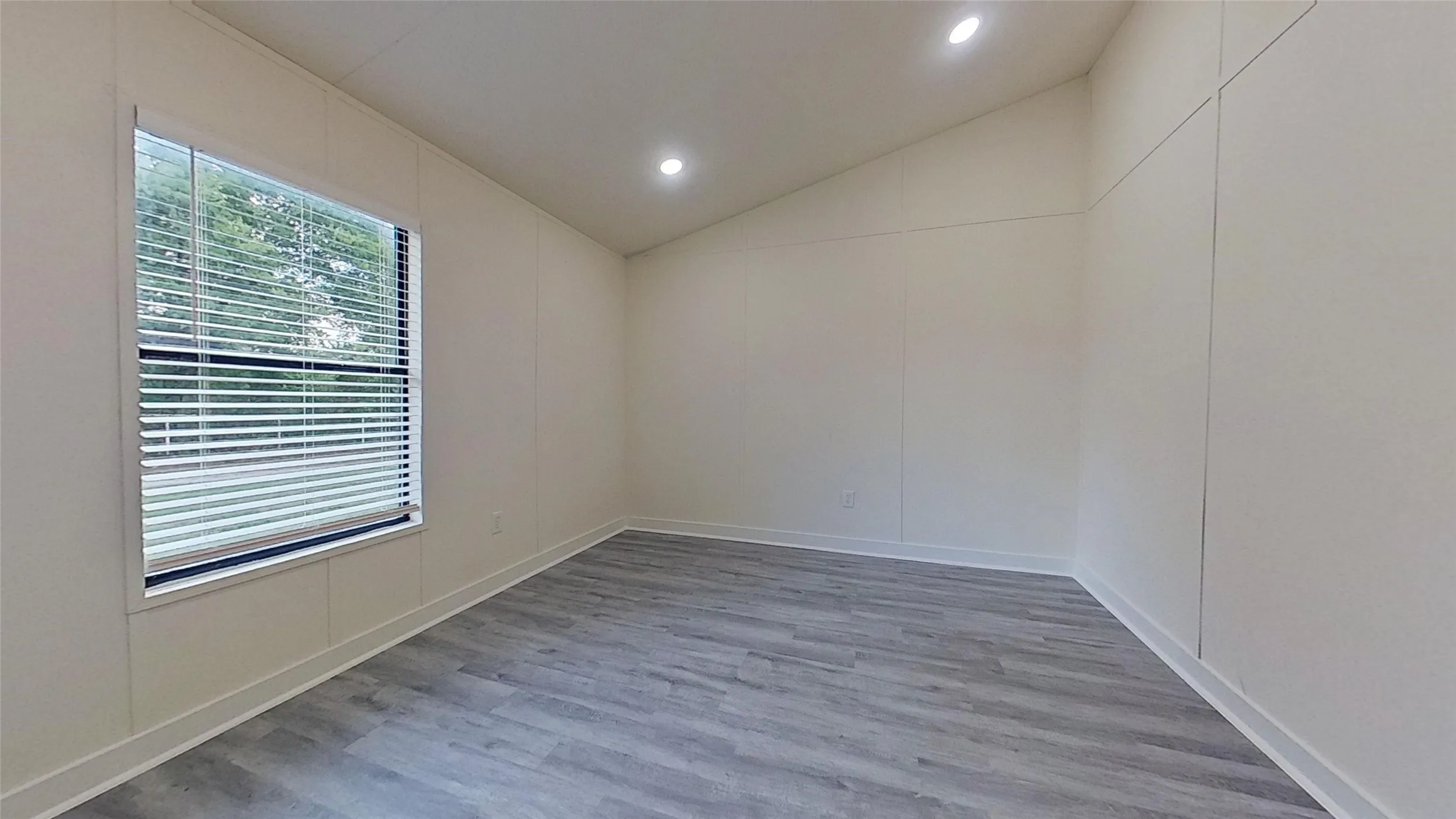 Room featuring vaulted ceilings, recessed lighting, a single window with blinds, panel-style walls, and wood-finish flooring