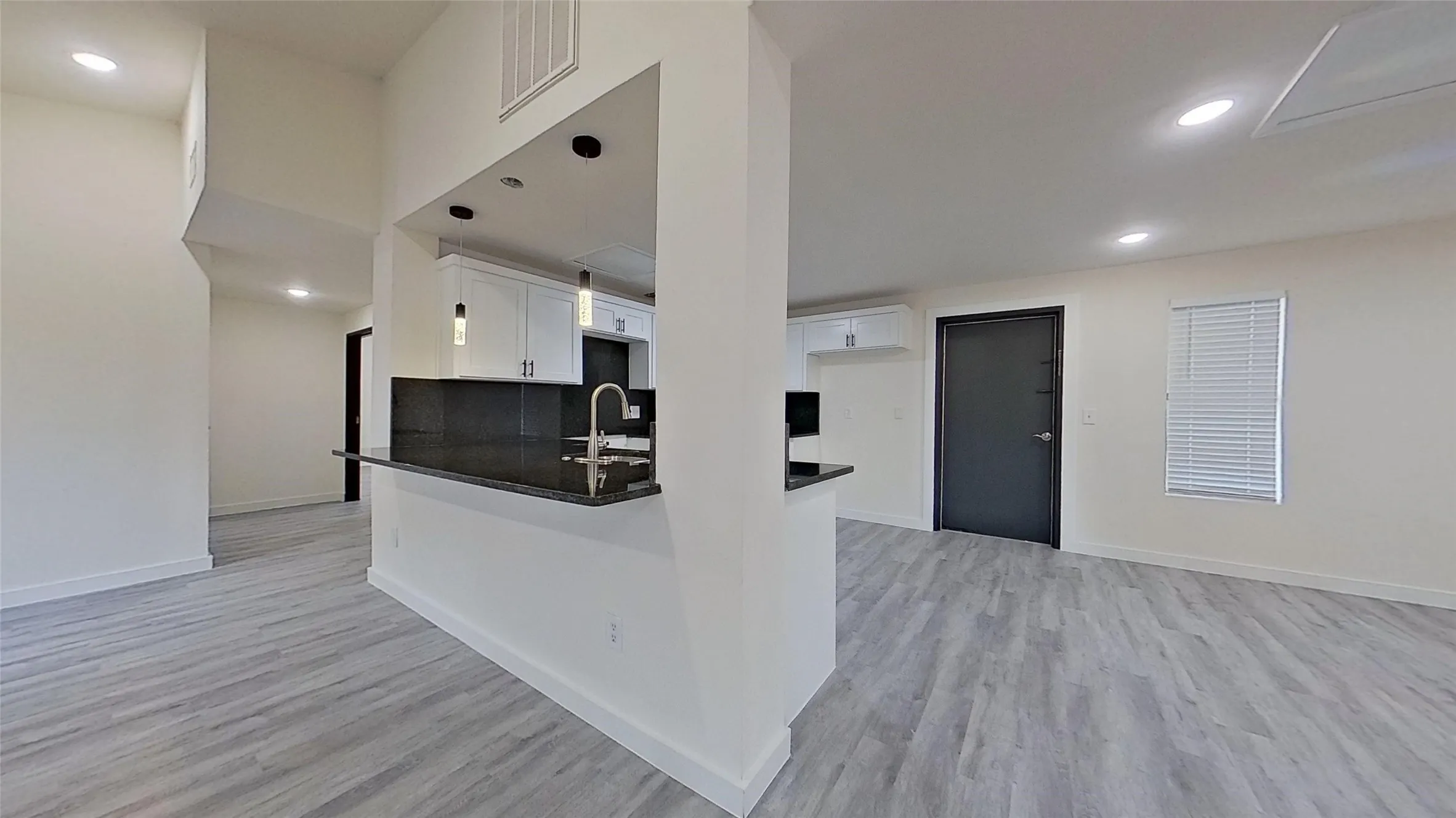 Open-concept living space featuring wood-finish flooring, recessed lighting, and a pass-through kitchen with a breakfast bar
