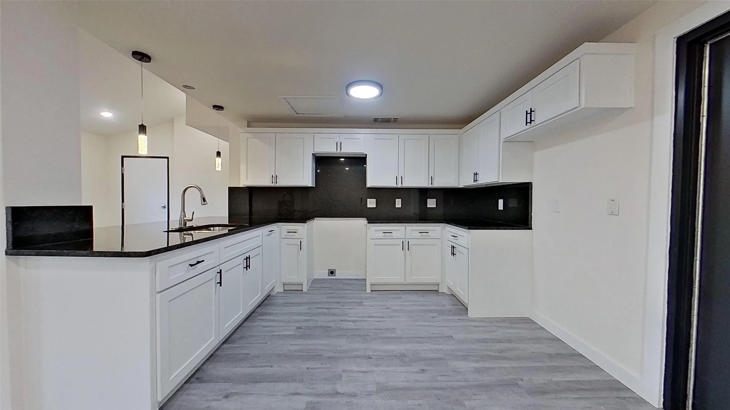 Kitchen featuring white shaker cabinetry, dark countertops, a stainless steel sink with a gooseneck faucet, gray wood-finish flooring, and pendant lighting