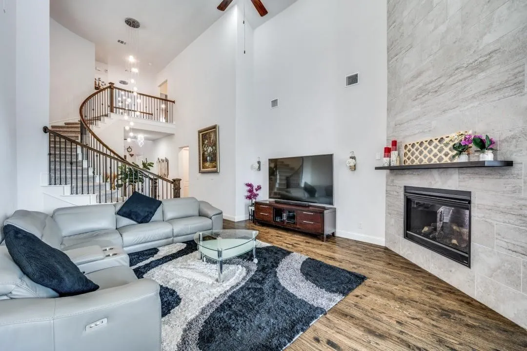 Two-story living area featuring wood-finish flooring, a contemporary fireplace with a stone surround, and a floating mantel
