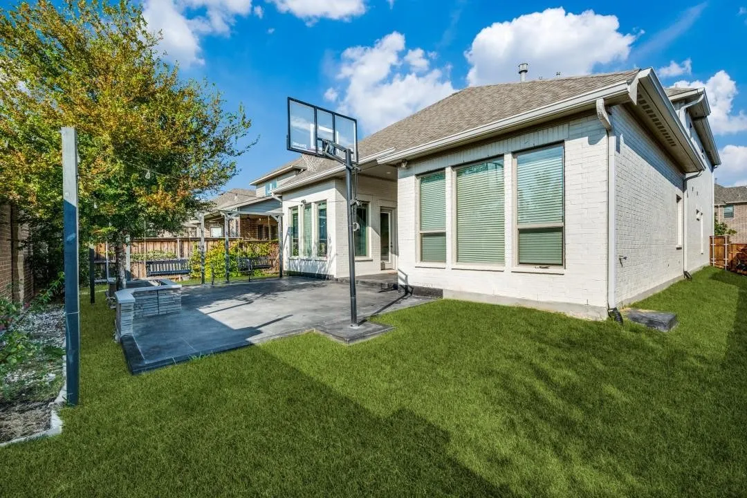 Expansive backyard featuring a manicured lawn, a large paver patio, a built-in stone bench, and an integrated basketball hoop