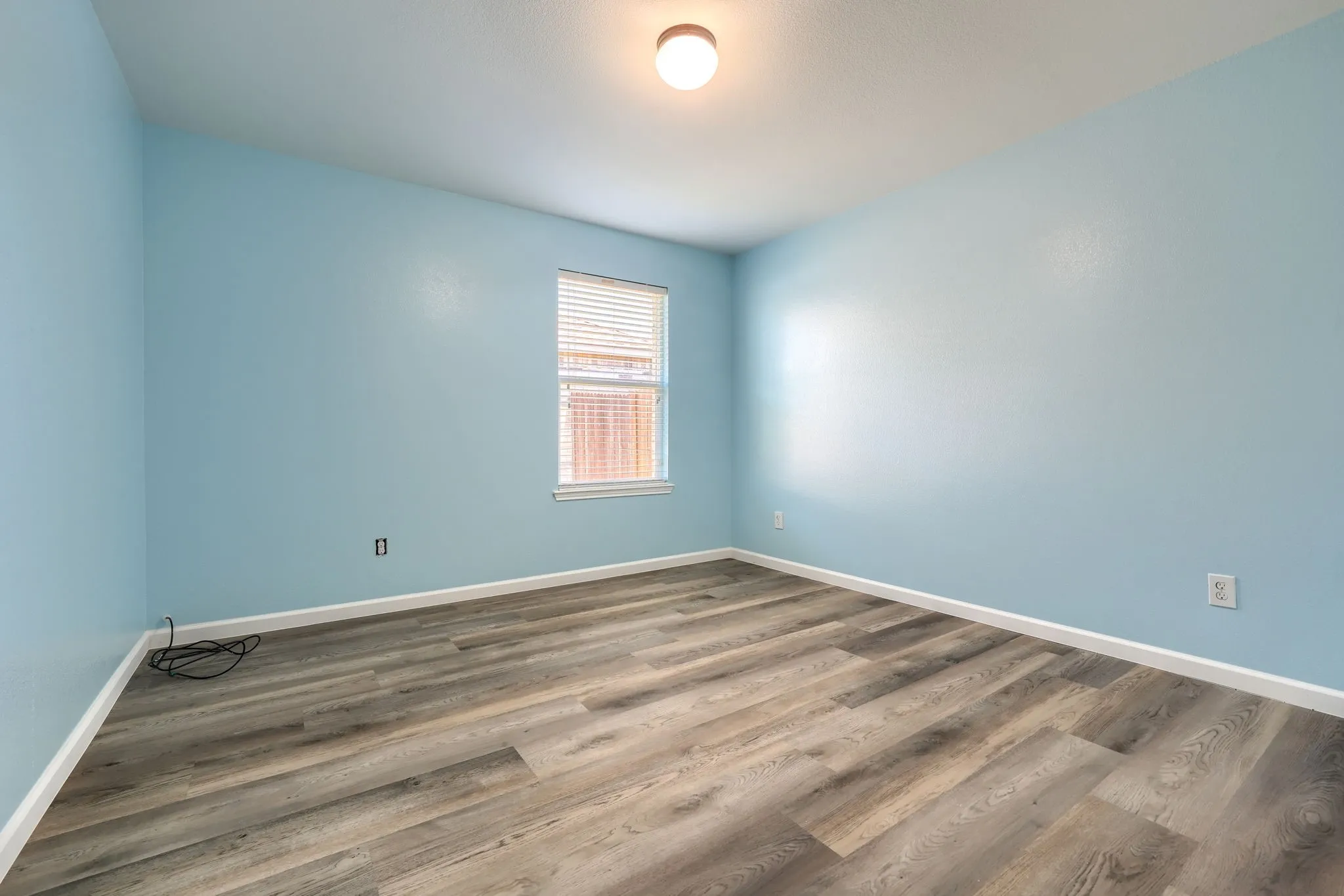 Room featuring wood-finish flooring, light blue walls, and a window with horizontal blinds