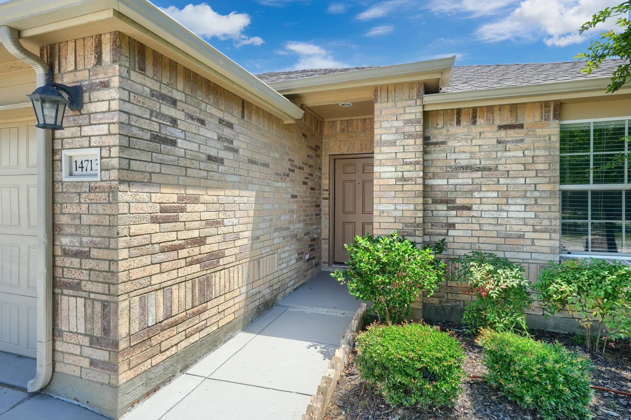 Brick exterior with a prominent entry door, an exterior light fixture, garage door, and a window with blinds