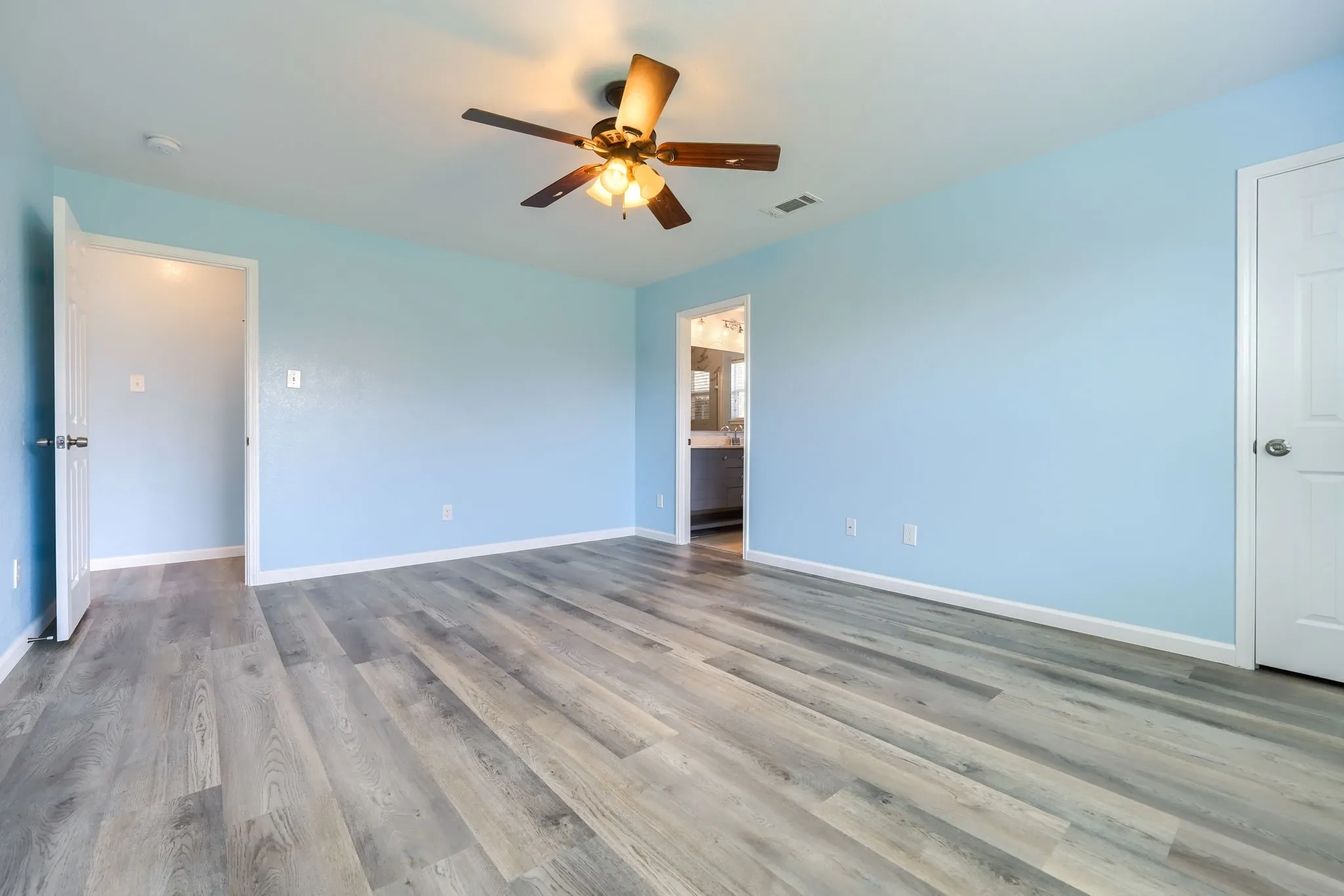 Spacious room featuring wood-finish flooring, light blue wall paint, white baseboards, and a ceiling fan with integrated lighting