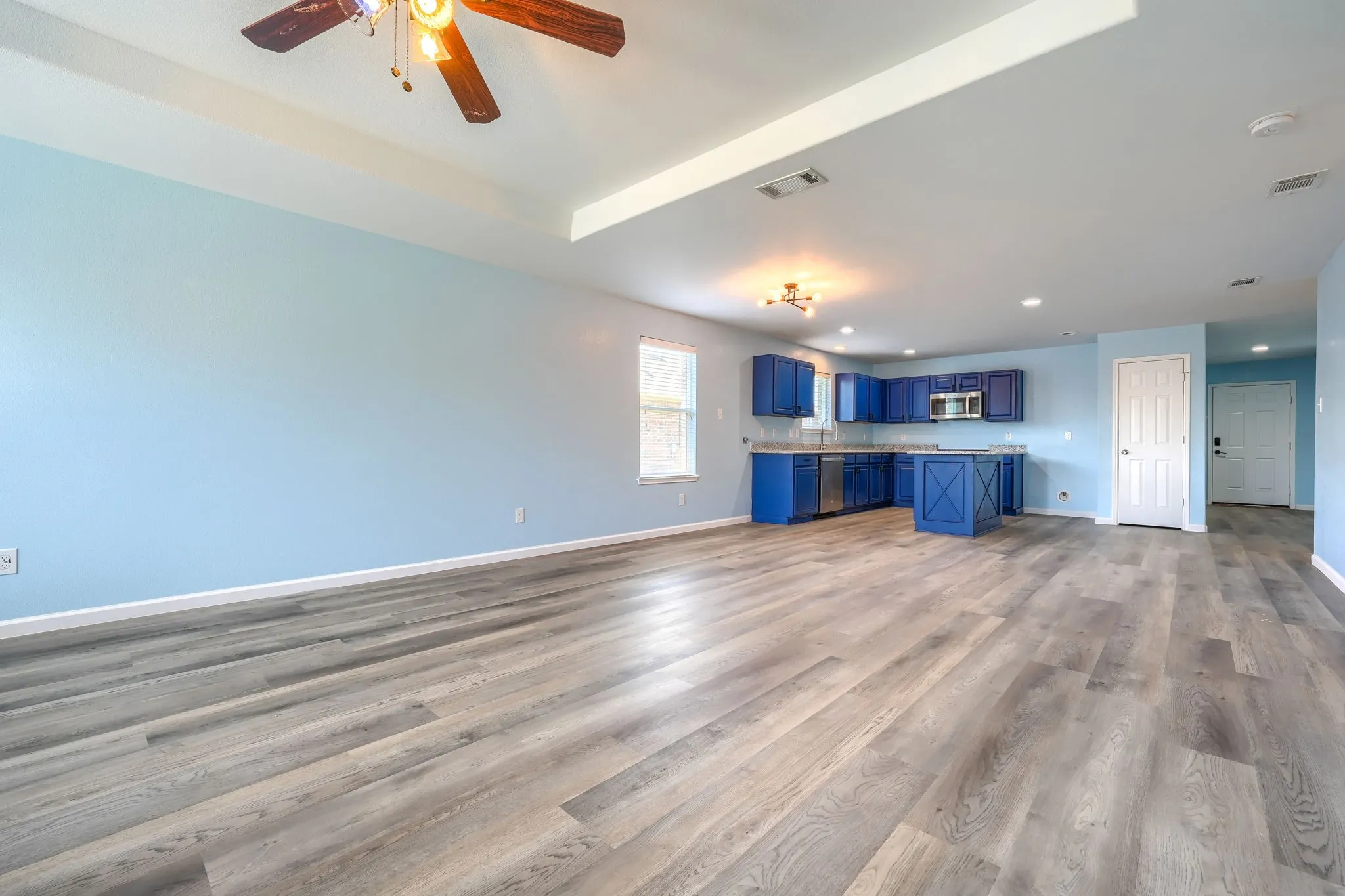 Open-concept interior featuring wood-finish flooring, light blue walls, and a recessed ceiling with a ceiling fan
