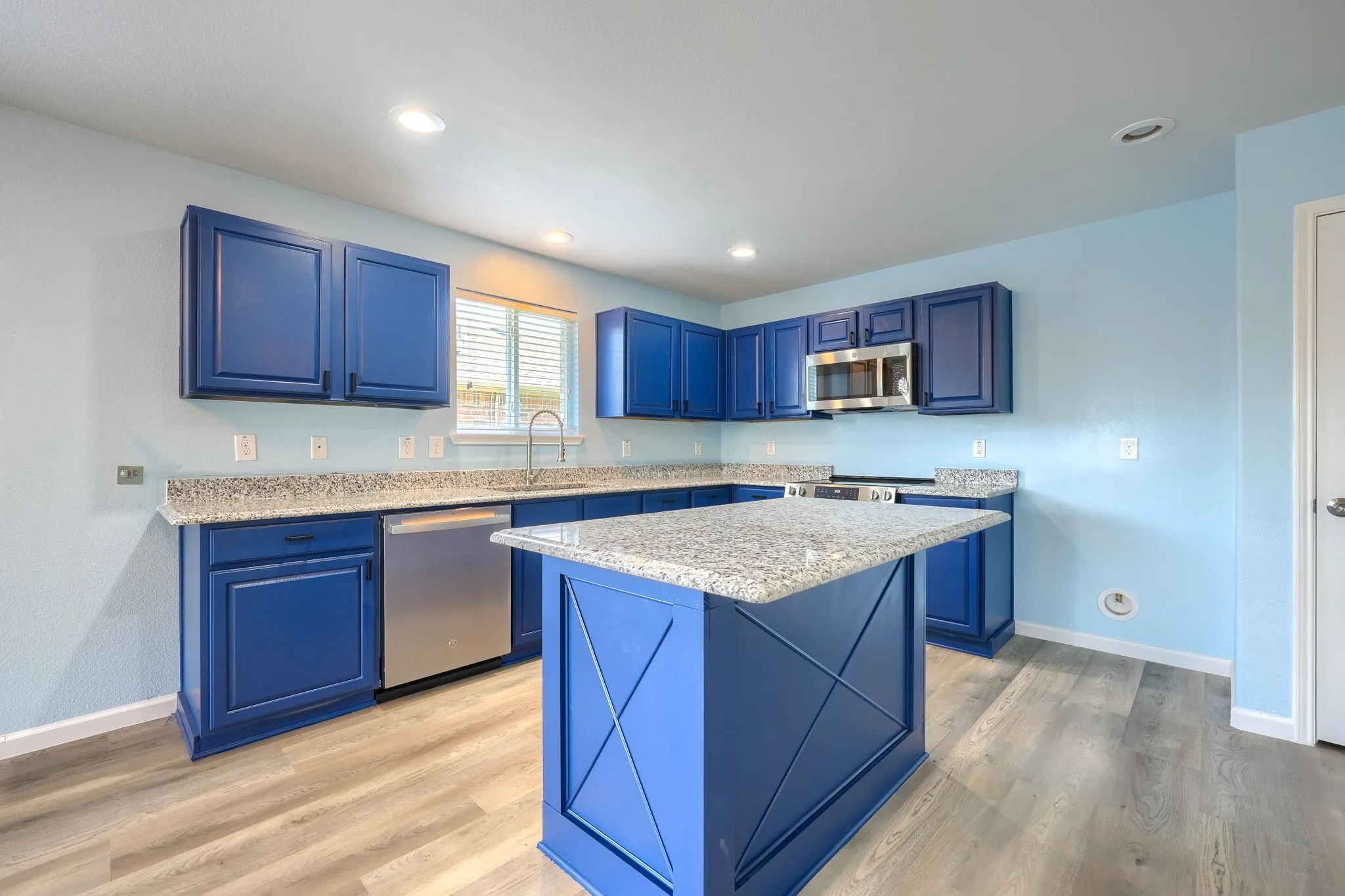 Kitchen featuring blue cabinetry, light granite countertops, stainless steel appliances, a center island, and wood-finish flooring