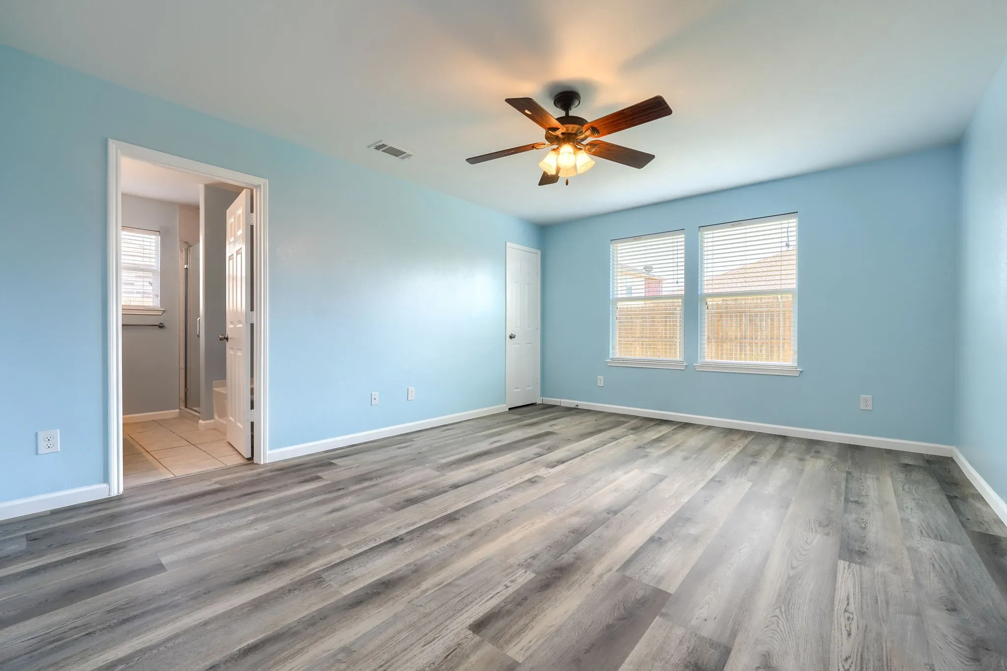 Spacious room featuring wood-finish flooring, light blue walls, and a ceiling fan with integrated lighting