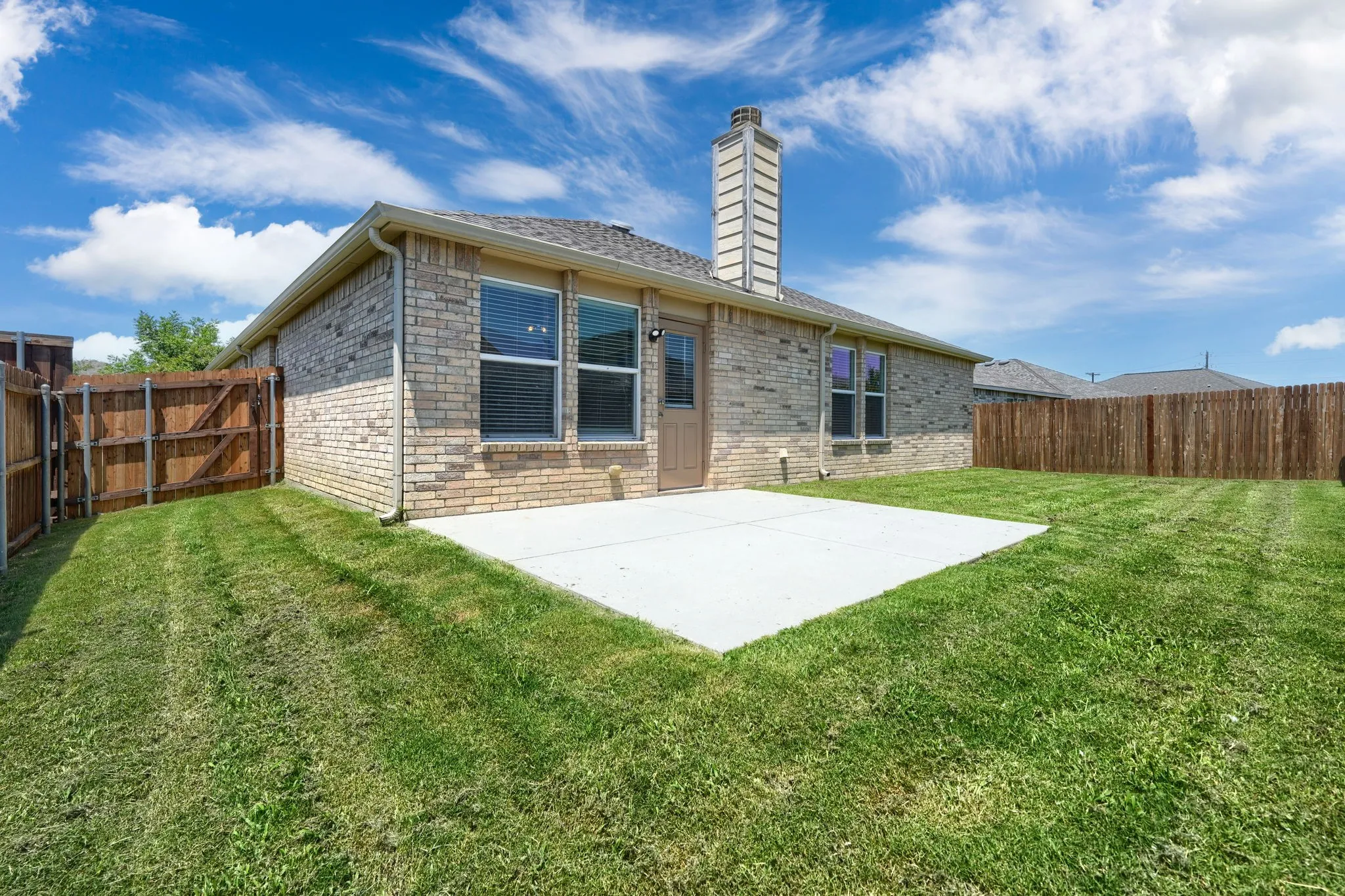 Expansive backyard featuring a large concrete patio, a brick exterior, a privacy fence, and a prominent chimney