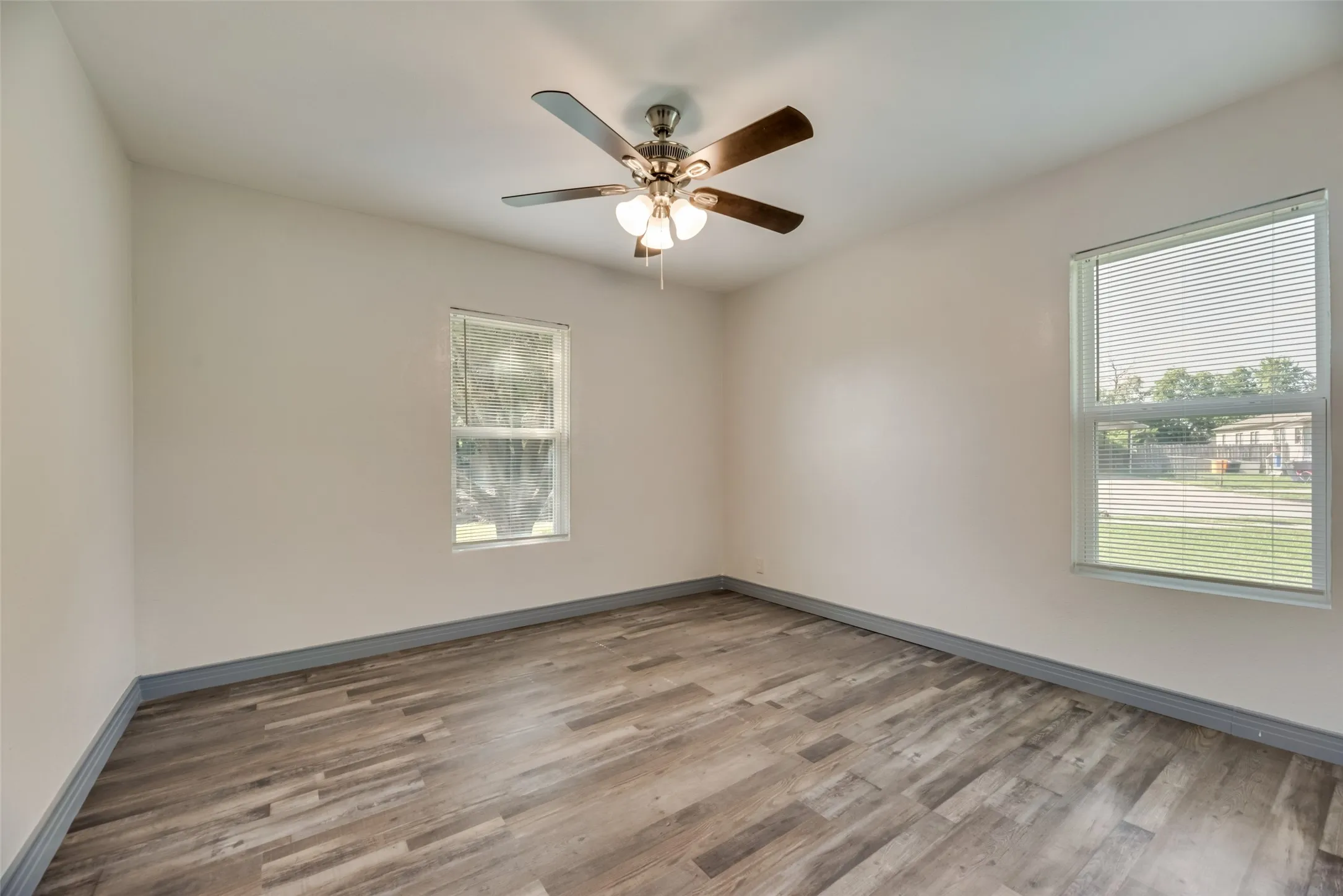 Spacious room featuring wood-finish flooring, light neutral wall paint, and a ceiling fan with integrated lighting