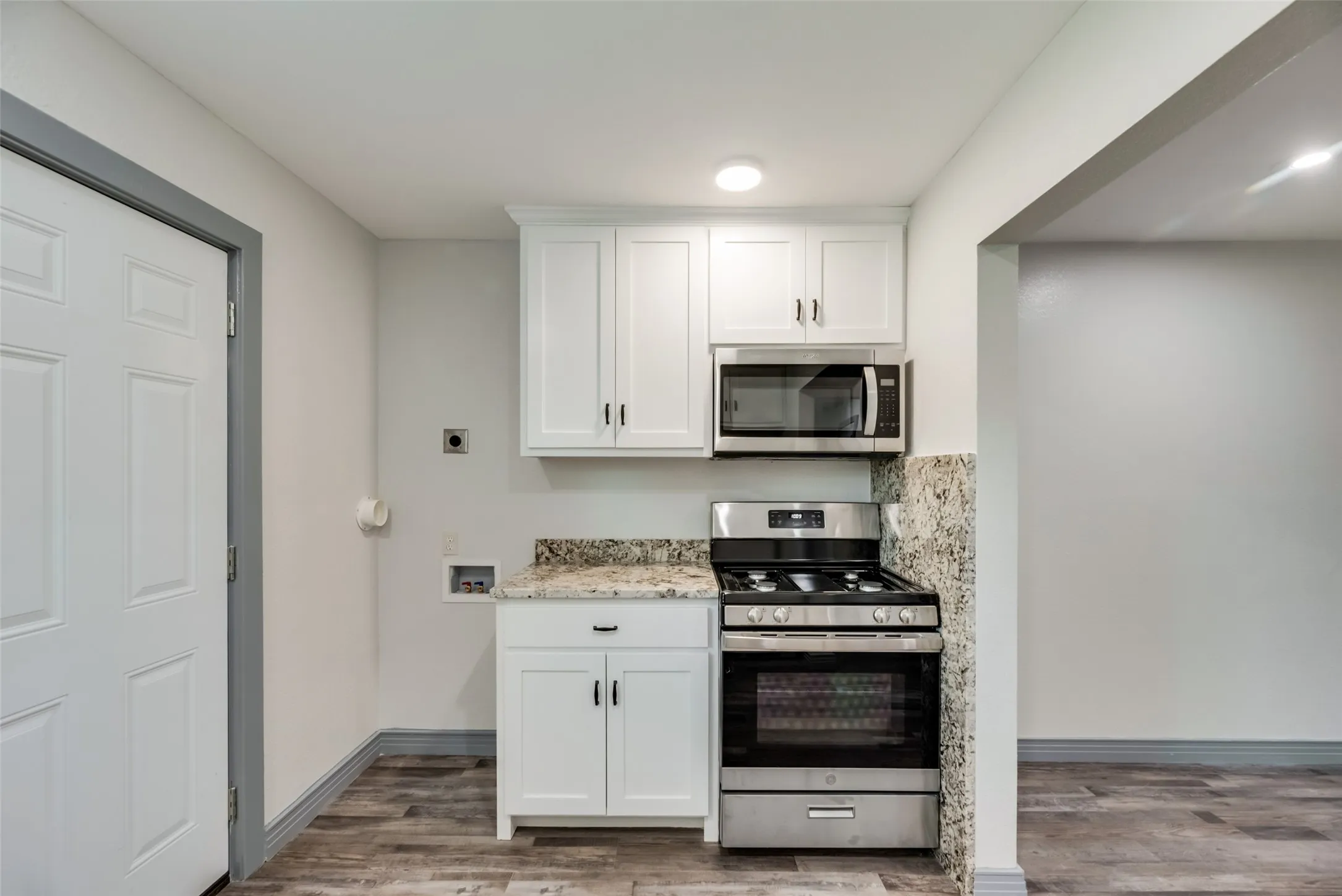 Compact kitchen area featuring white shaker-style cabinetry, a built-in stainless steel microwave, and a stainless steel range with an oven