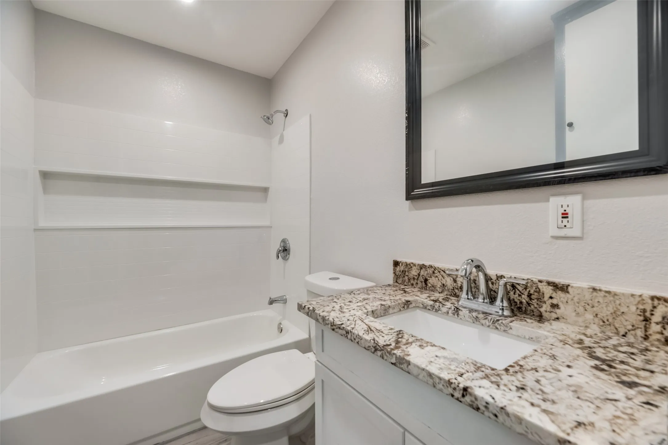 Bathroom featuring a white bathtub, shower with built-in shelving, white vanity with a granite countertop, and chrome fixtures