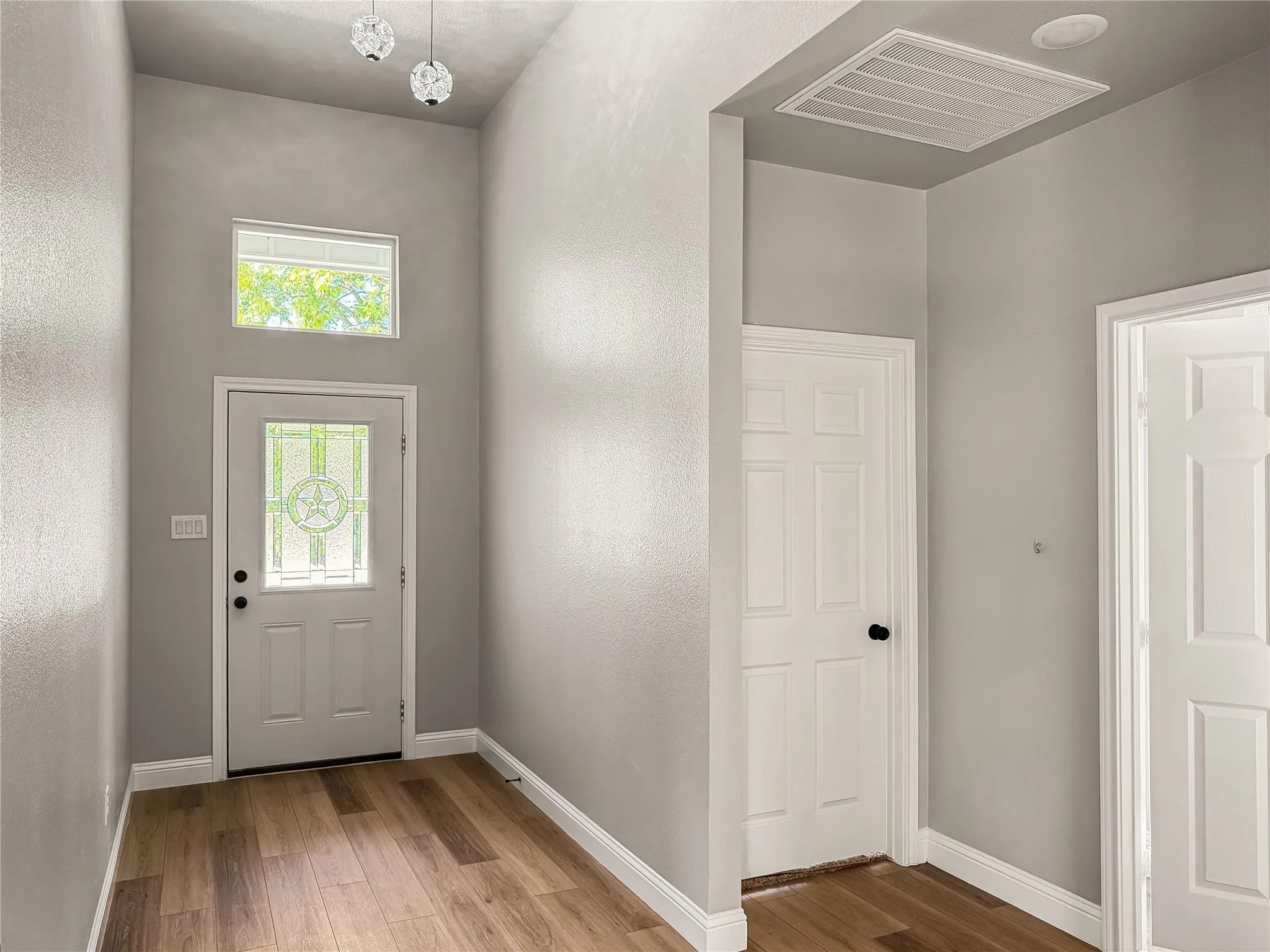 Entryway featuring wood-finish flooring, a white paneled door with decorative glass, a transom window, and two pendant light fixtures
