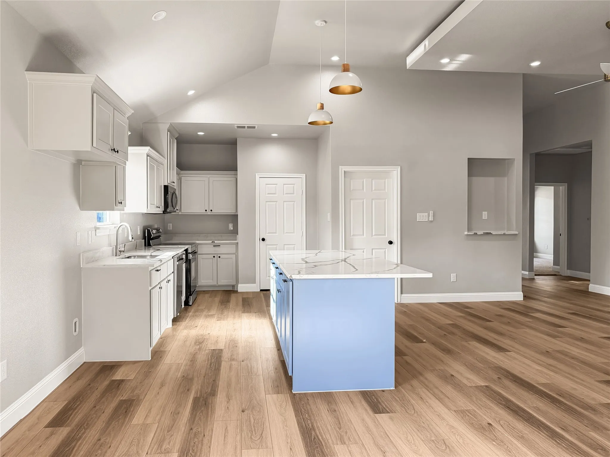 Open-concept kitchen featuring white cabinetry, light countertops, stainless steel appliances, wood-finish flooring, and a central island with pendant lighting