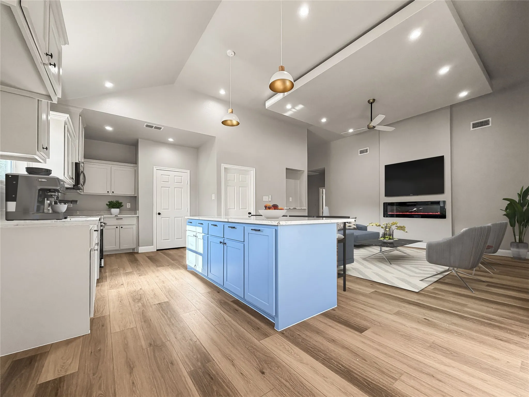 Expansive living space featuring wood-finish flooring, a kitchen island with light blue cabinetry, white shaker-style kitchen cabinets, an integrated wall-mounted fireplace, and recessed lighting