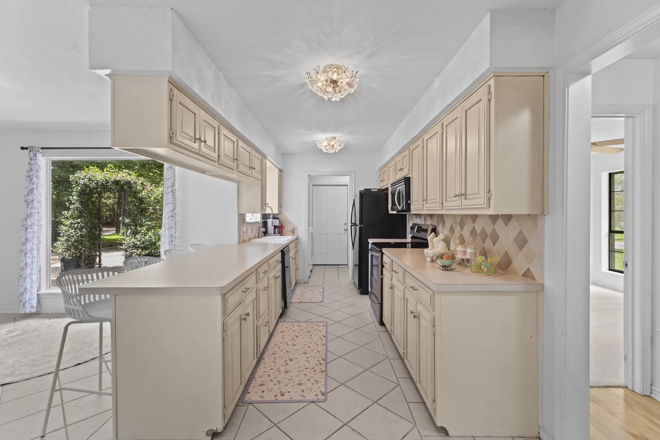 Galley kitchen featuring light cabinetry, full-size black appliances, and a tiled backsplash