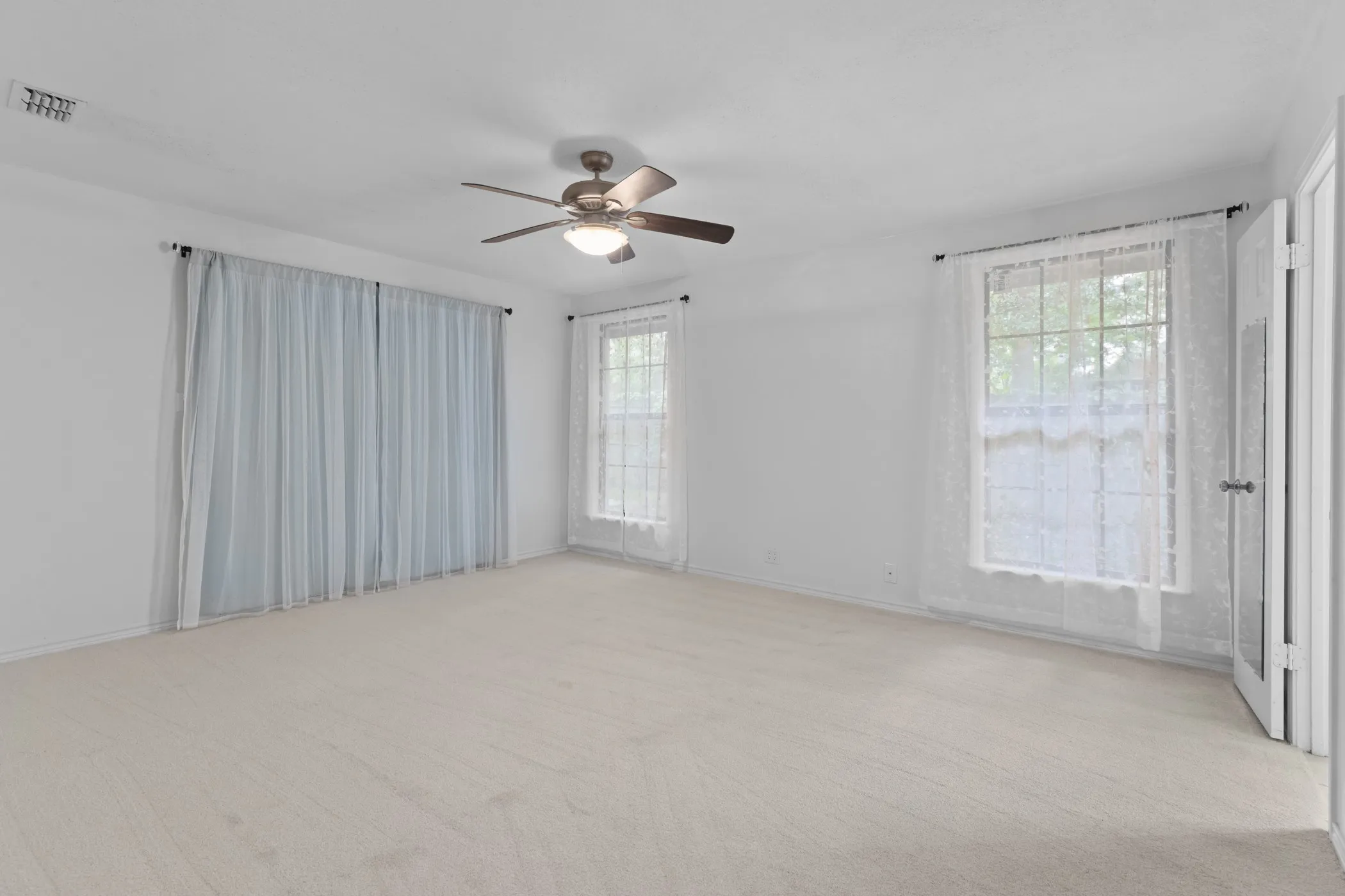 Neutral tone wall paint, light-toned carpet, a ceiling fan with integrated lighting, and two windows allowing natural light