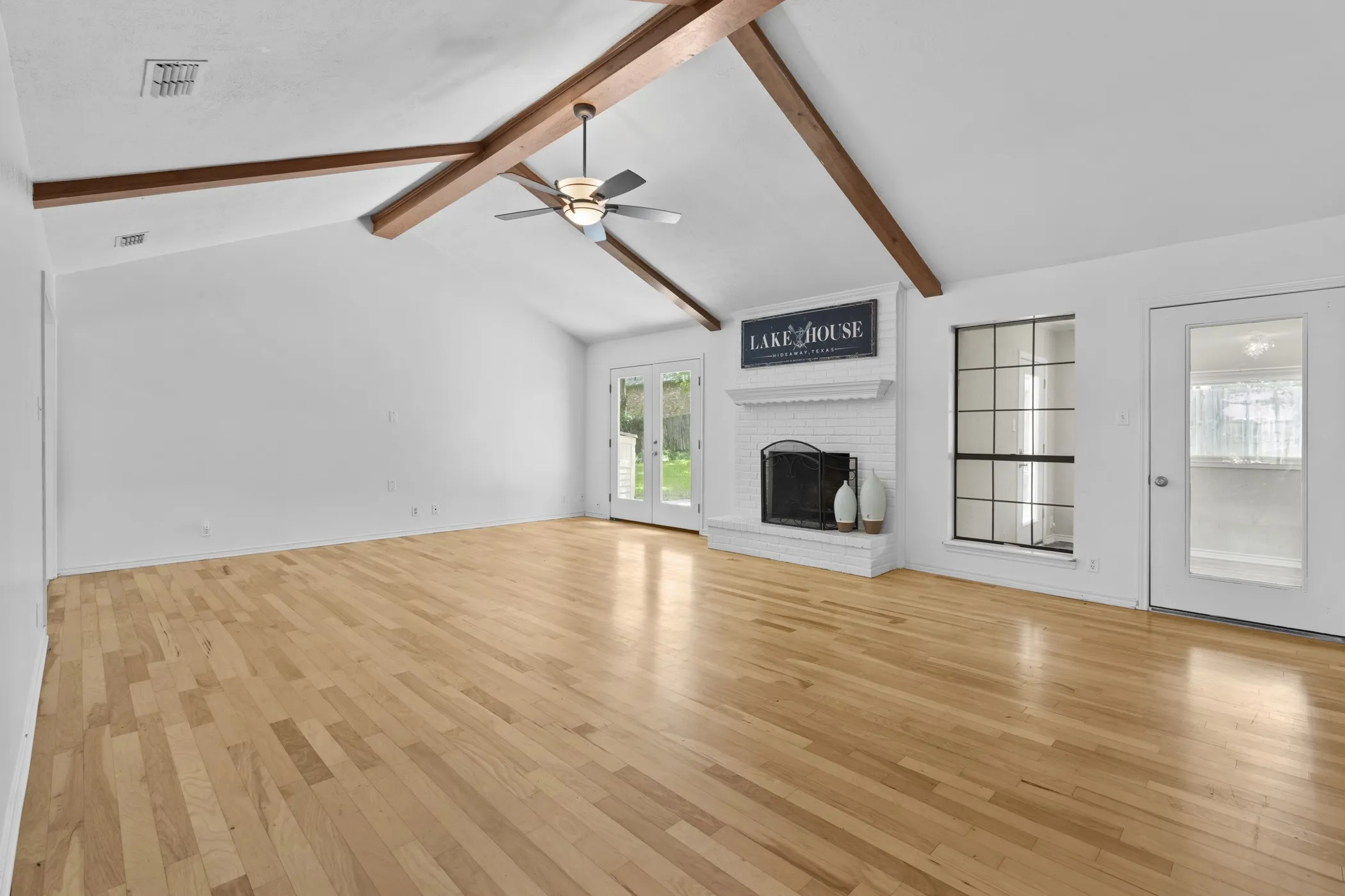 Vaulted ceilings with exposed wood beams, light wood-finish flooring, and a white brick fireplace with a mantel