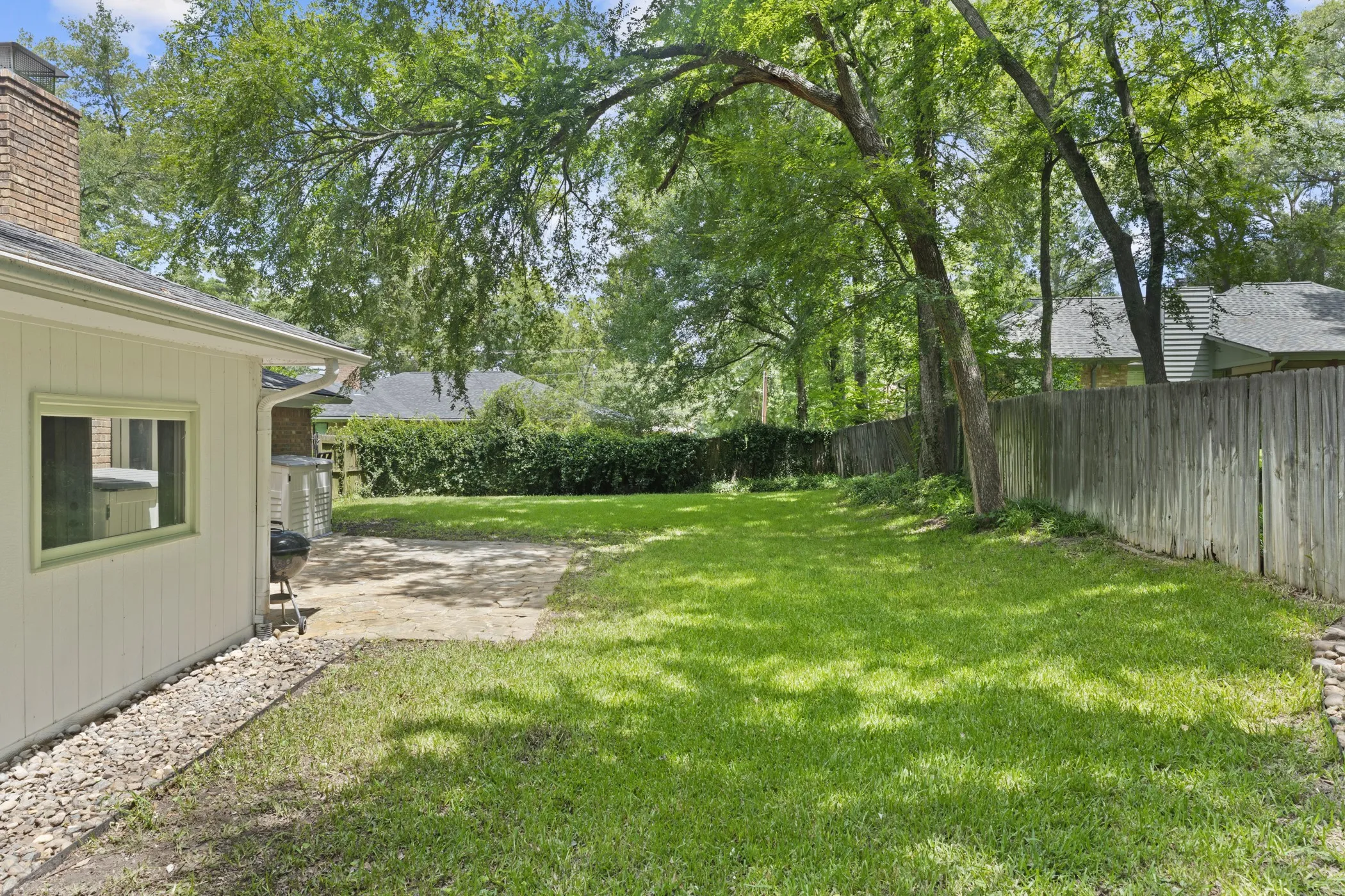 Expansive backyard featuring a green lawn, mature trees, a privacy fence, and a stone patio
