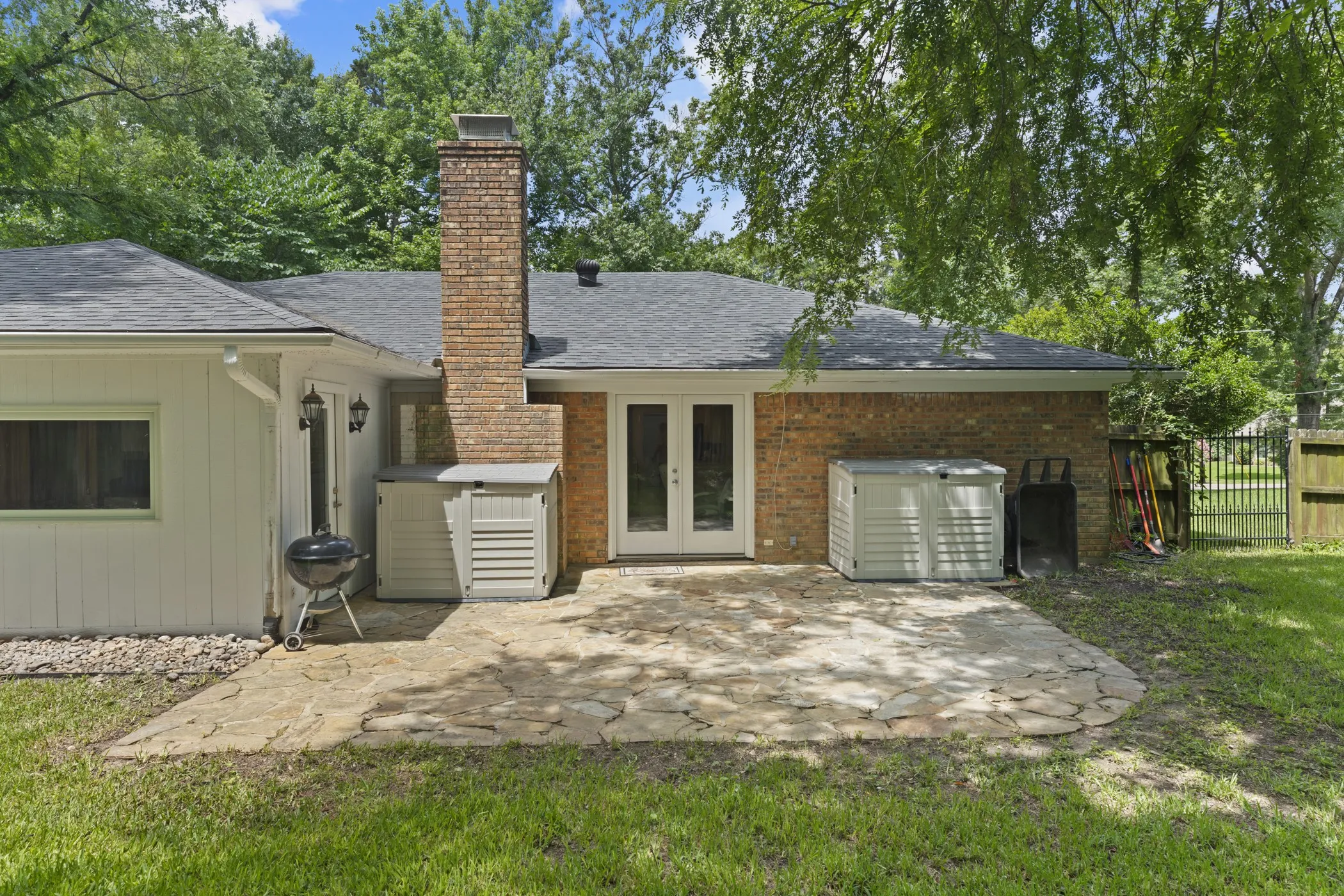 Stone patio with a brick exterior, double glass panel doors, and a brick chimney