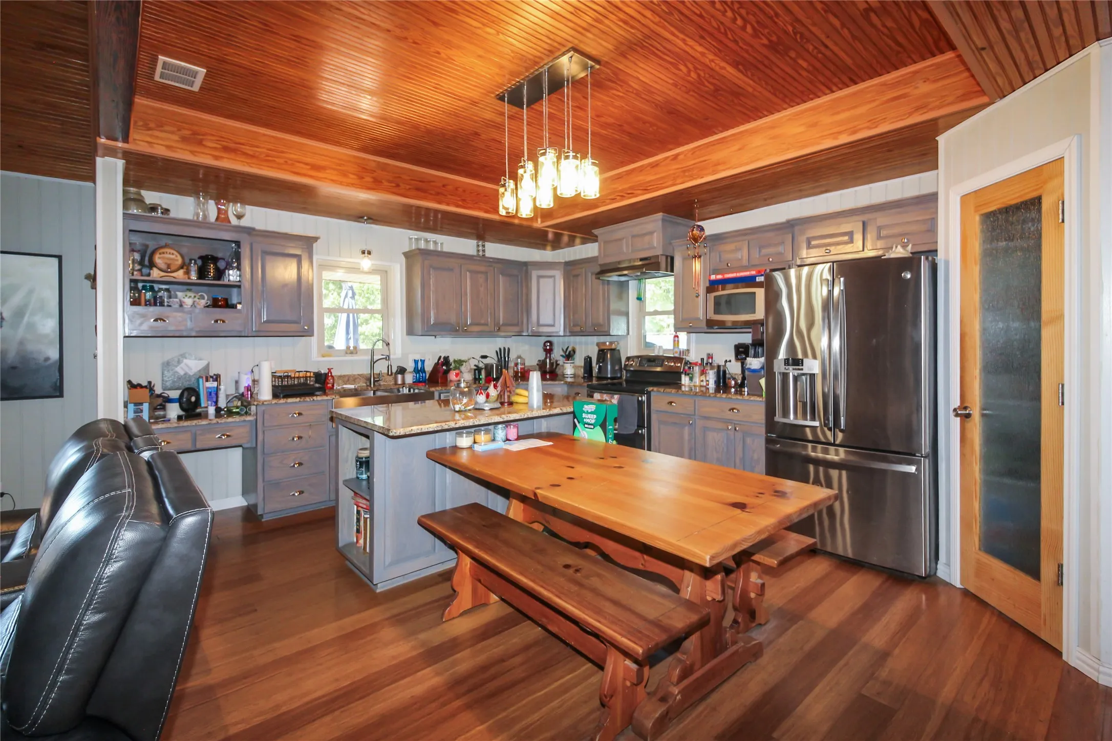 Kitchen featuring wood-finish flooring, exposed wood beam ceiling, stainless steel appliances, grey cabinetry, and a central island with a stone countertop