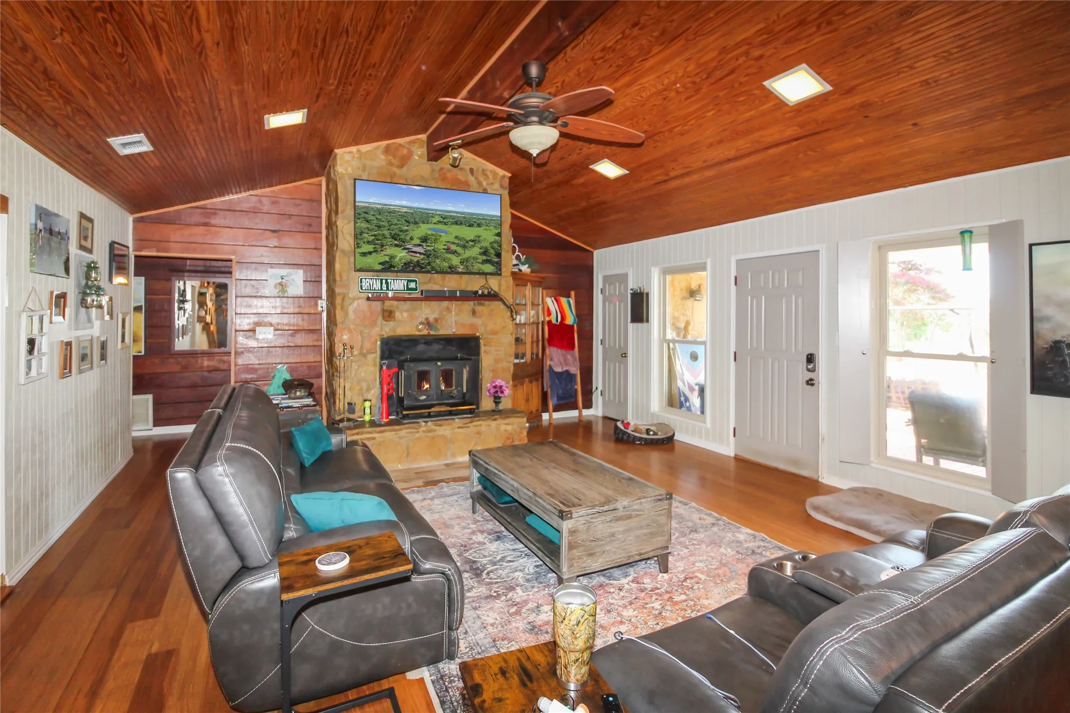 Living area featuring a stone fireplace with hearth, wood-finish flooring, and a vaulted wood-paneled ceiling