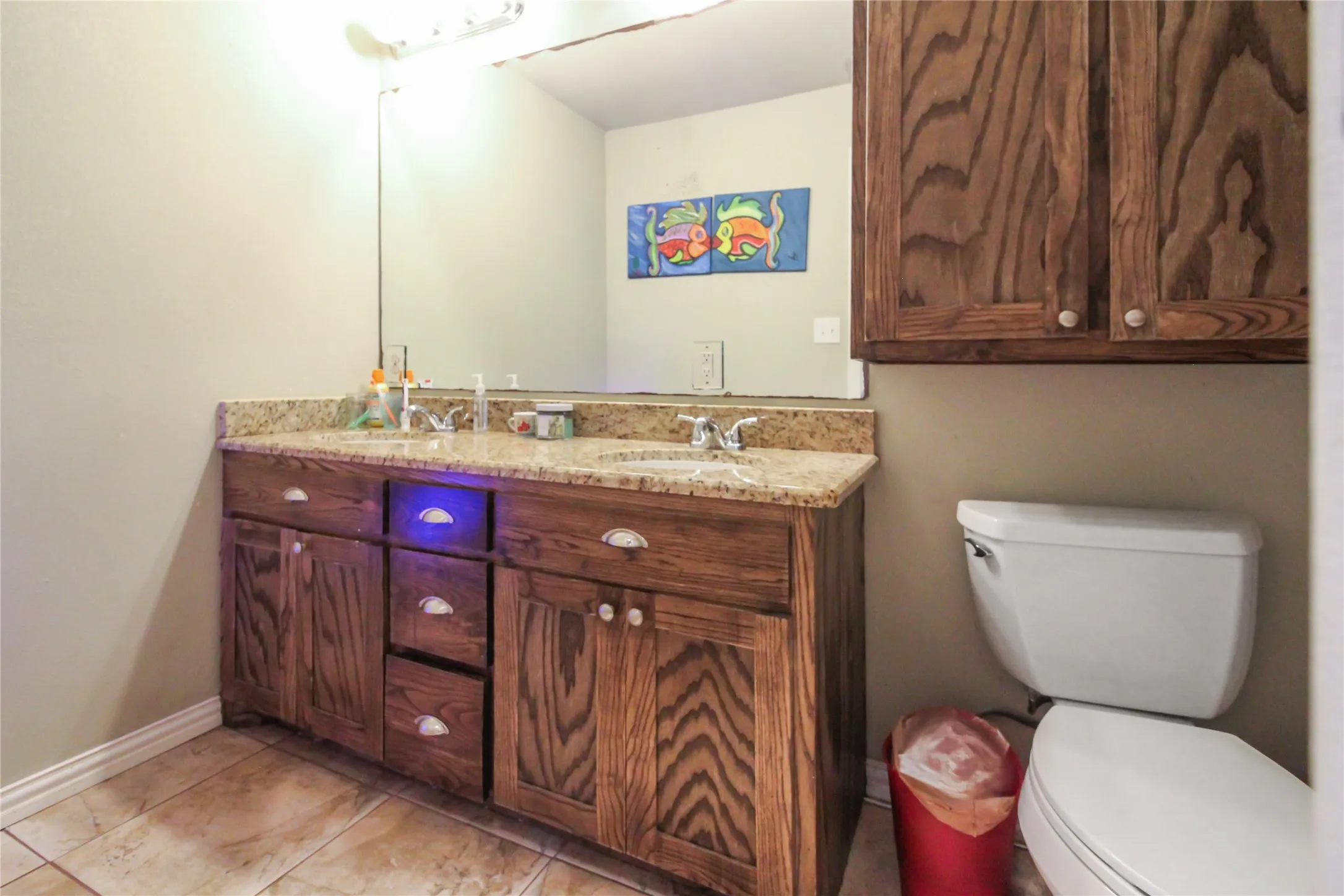 Double wood-finish vanity with granite-style countertop, dual sinks, and under-cabinet storage