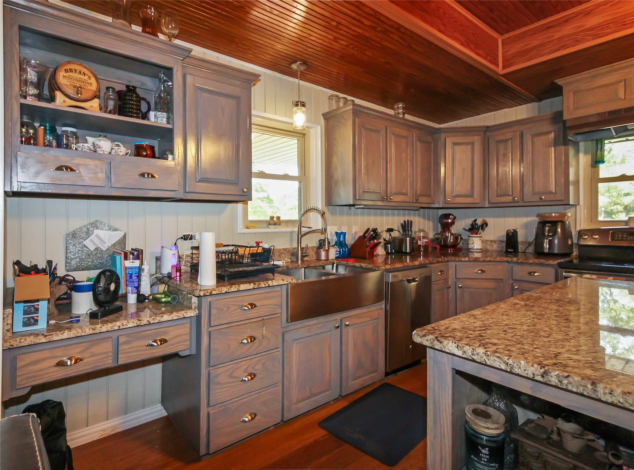 Kitchen featuring warm wood-finish plank ceiling, perimeter cabinetry with open shelving, granite countertops, and a stainless steel farmhouse sink