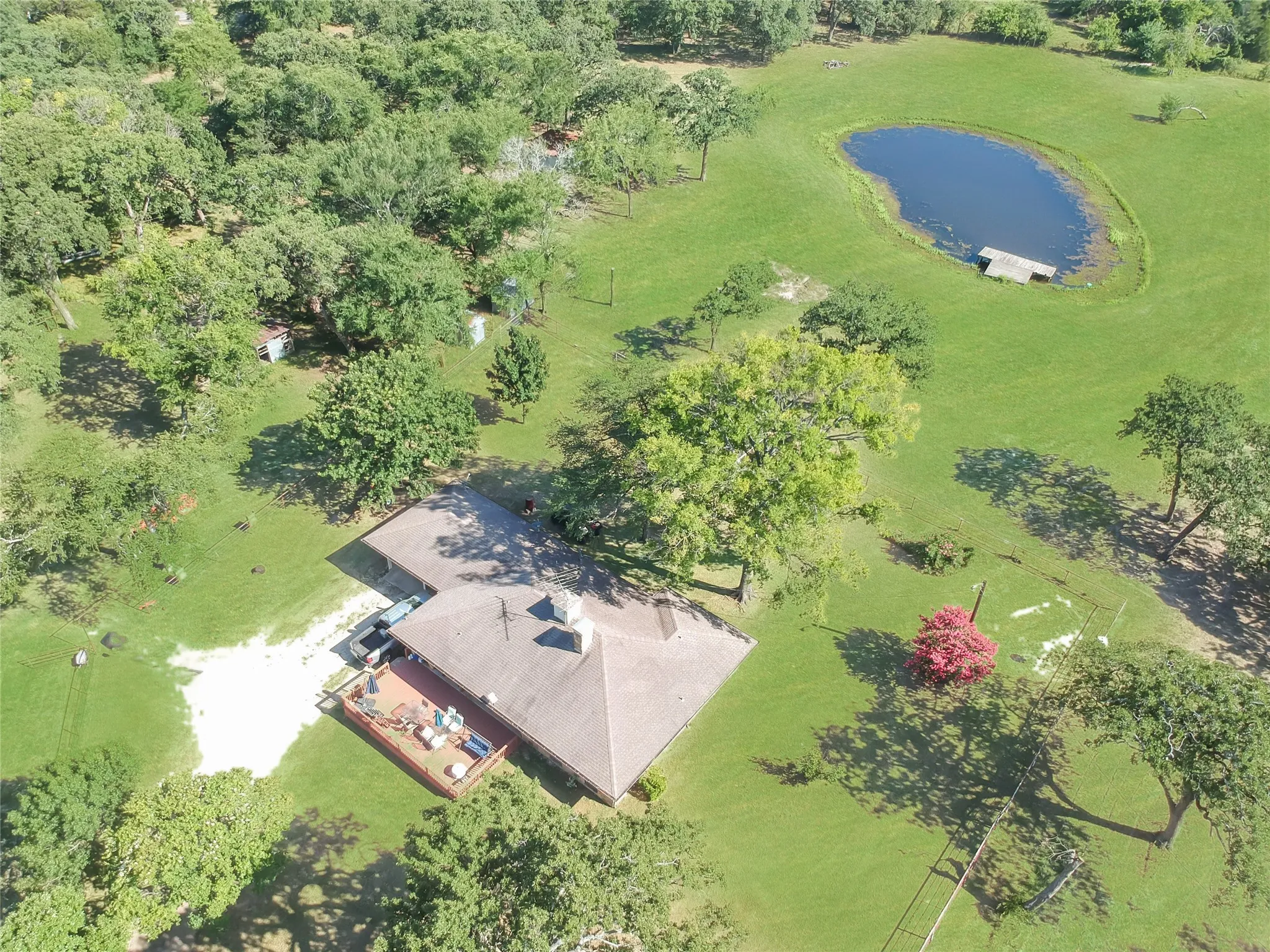 Expansive grounds featuring a private pond with a small dock, mature trees, and a sprawling residence with a large outdoor deck