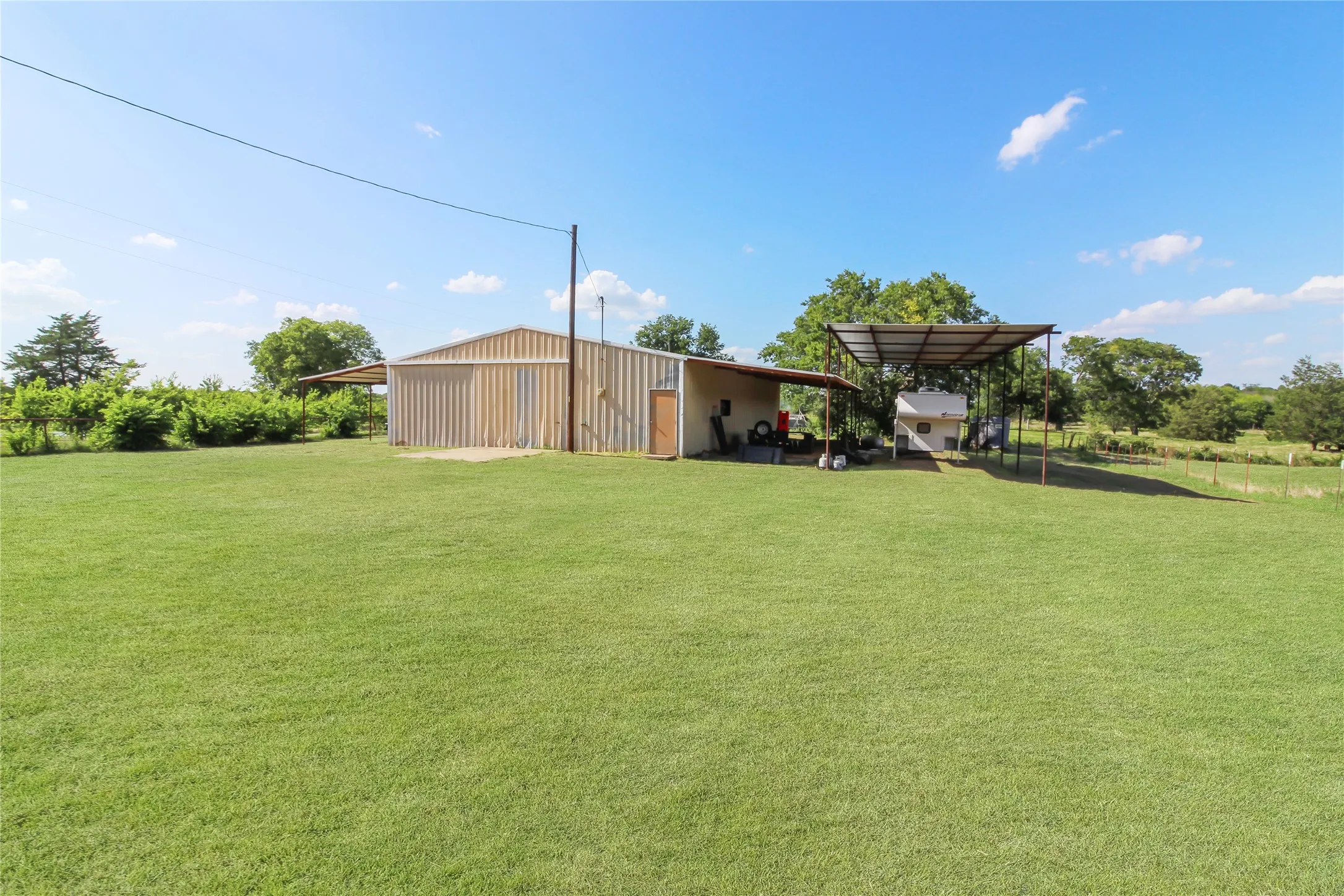 Expansive green lawn with a large utility building featuring metal siding and an attached covered carport structure