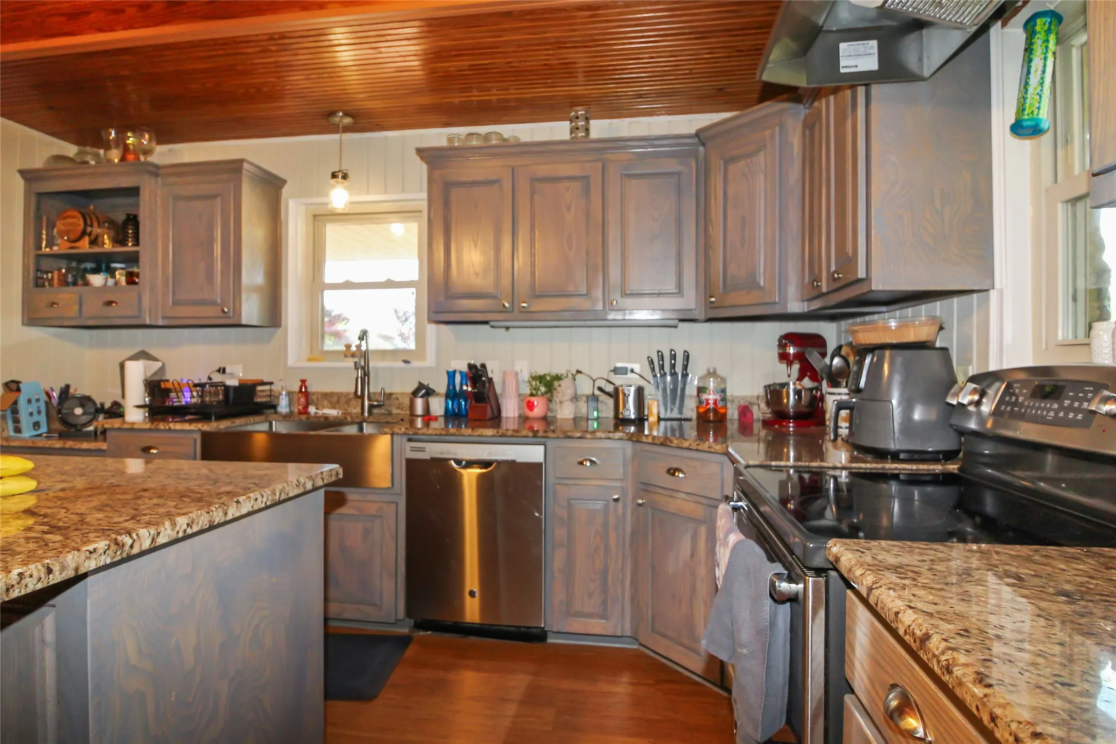 Kitchen featuring wood-finish cabinetry, granite countertops, stainless steel appliances, a farmhouse-style sink, and a beadboard backsplash