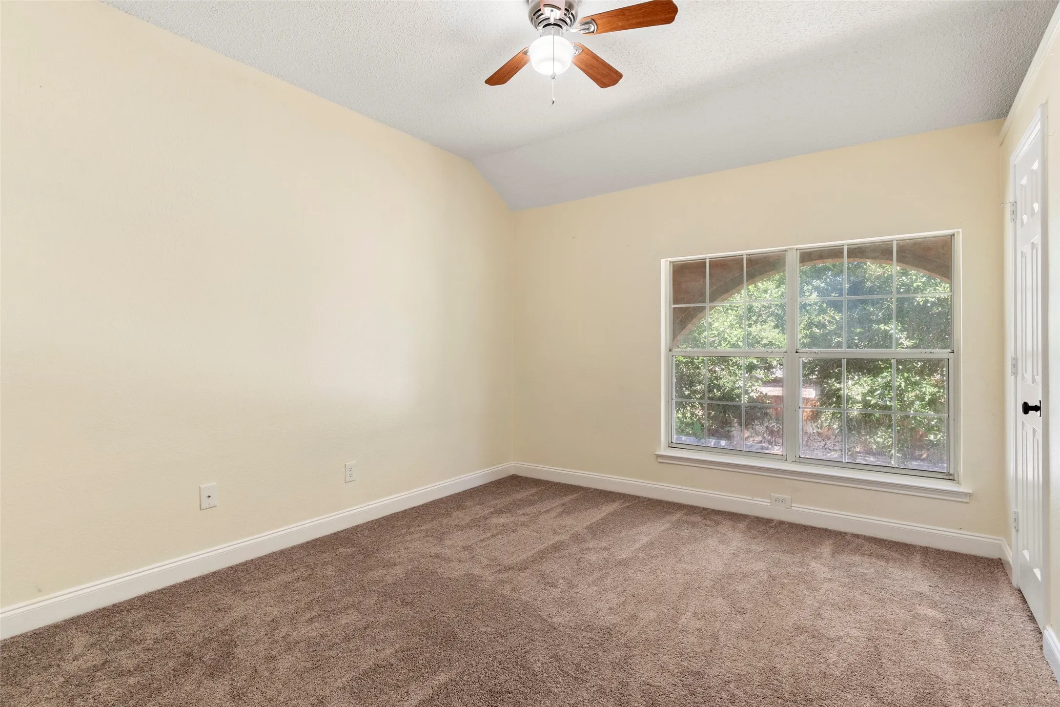 Carpeted room featuring a vaulted ceiling with a ceiling fan, a large arched window, and white trim