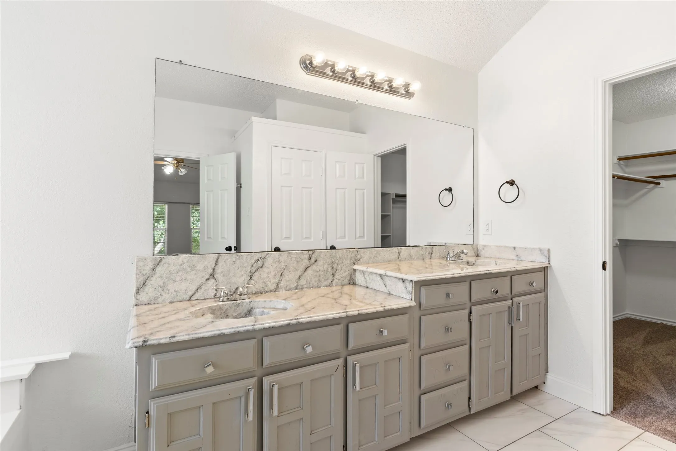 Double vanity featuring stone countertops with integrated sinks, light gray cabinetry, and a full-width wall mirror