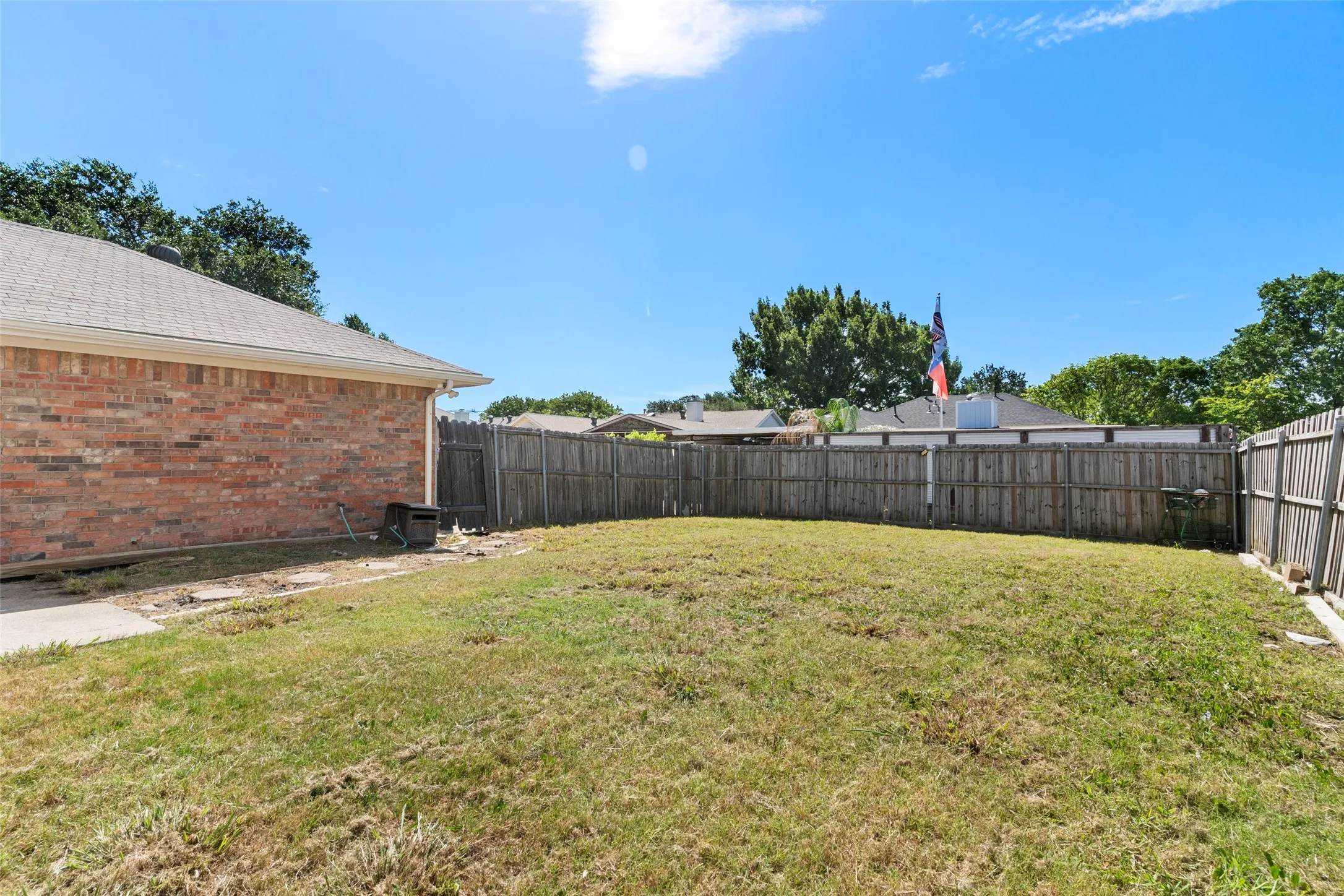 Expansive backyard featuring a wood privacy fence, a brick exterior wall, and a concrete pathway