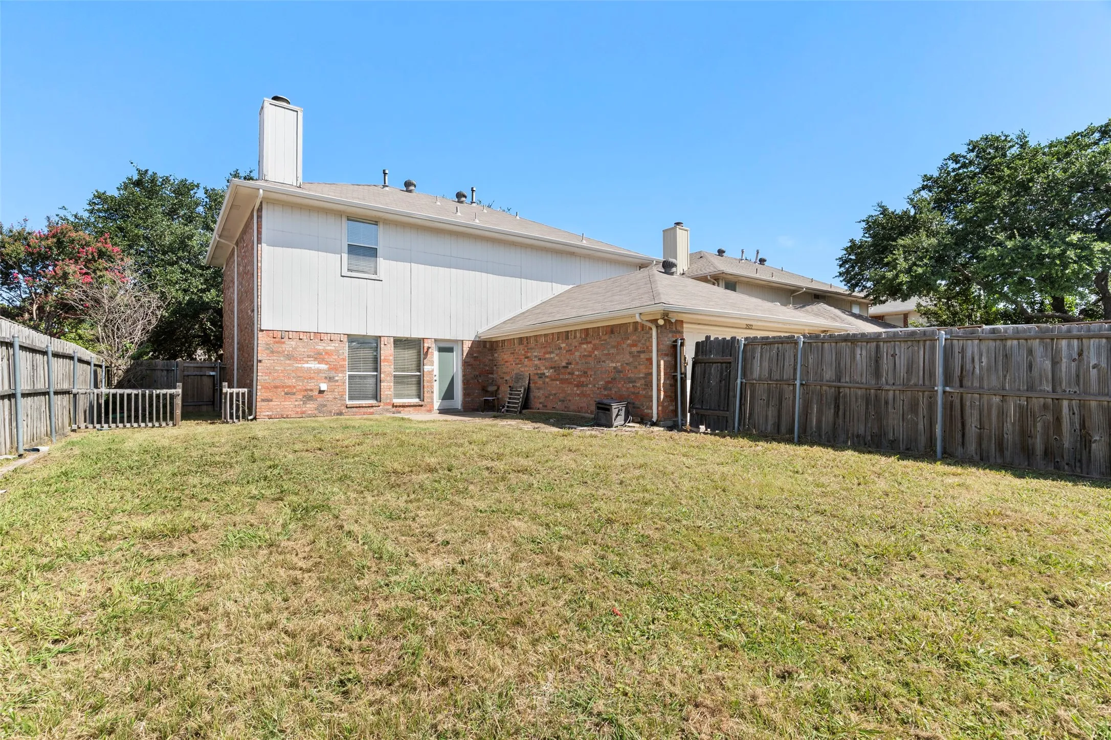 Expansive backyard featuring a privacy fence, brick and siding exterior, multiple windows, and a rear entry door