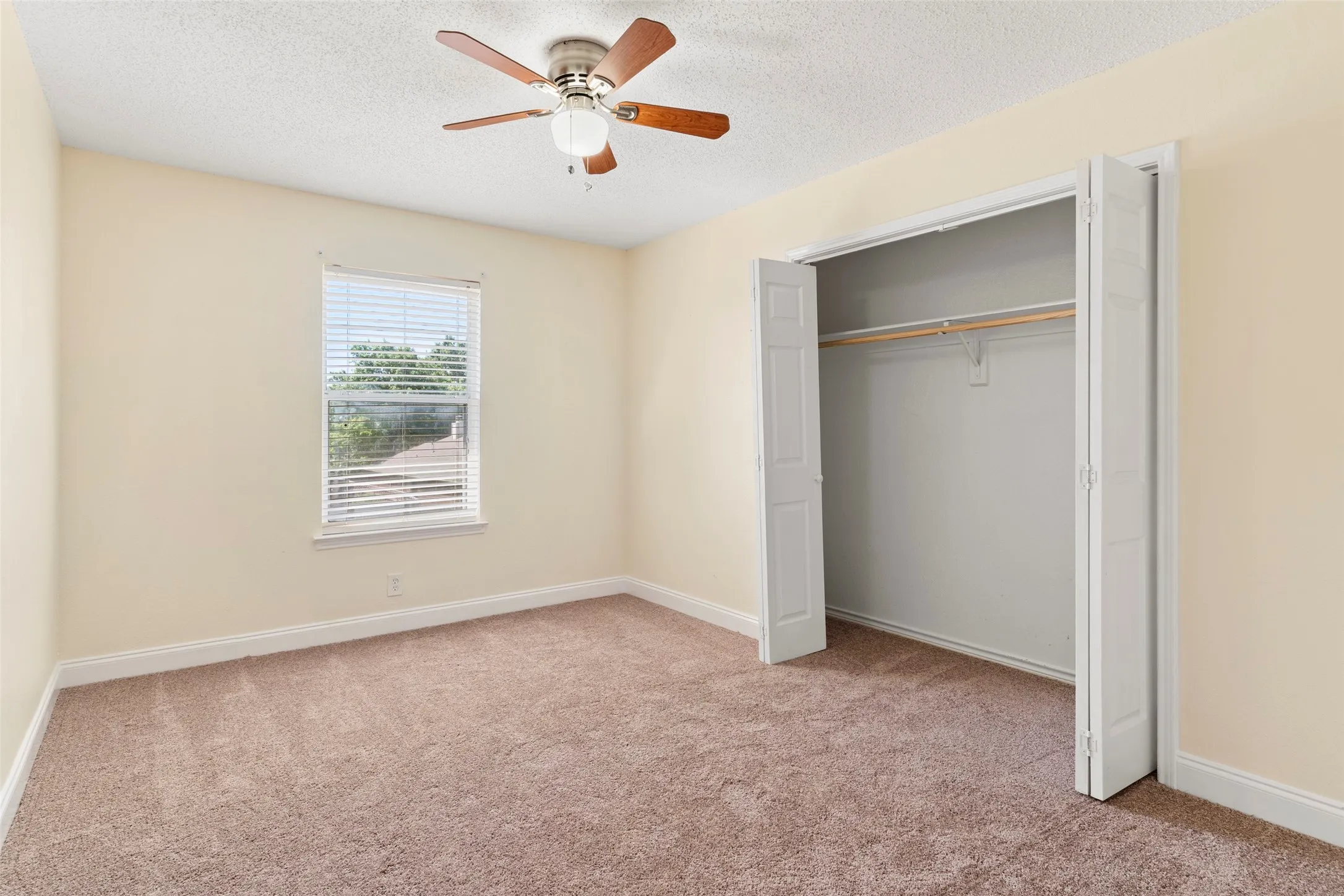 Carpeted room featuring a ceiling fan with light fixture, a window with horizontal blinds, and a bi-fold door closet with a hanging rod