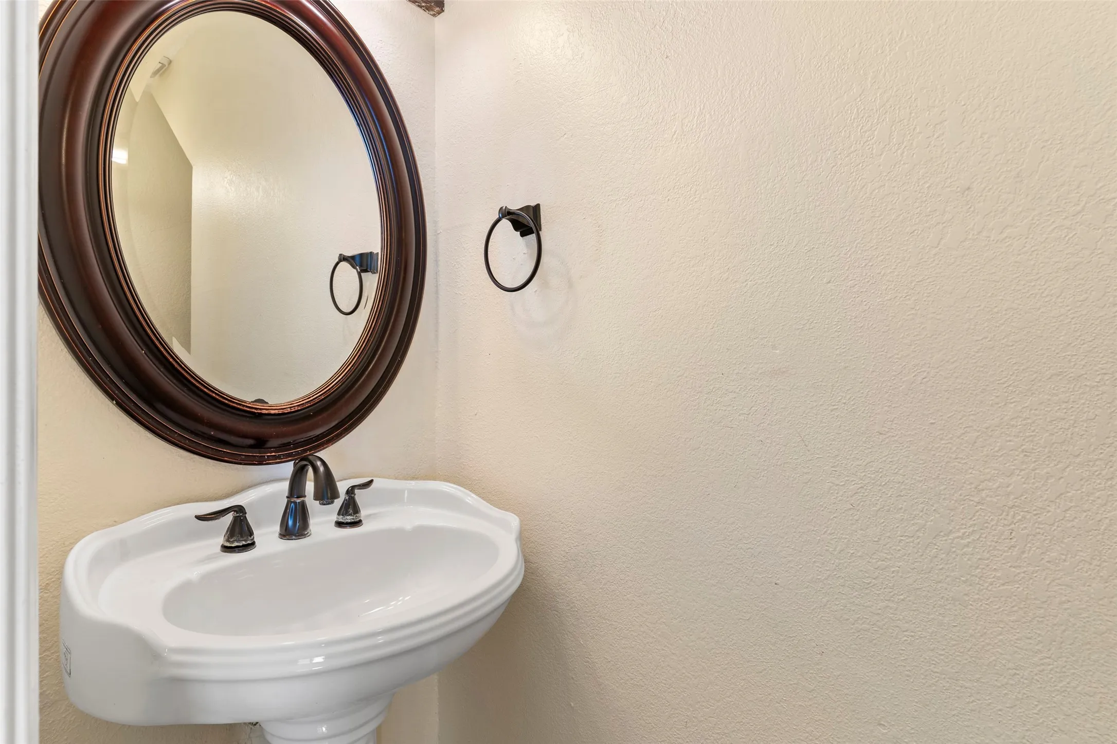 Pedestal sink with black faucet and fixtures, paired with a dark wood-framed oval mirror